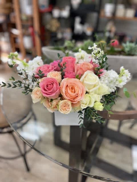 Pink and peach roses arranged with white flowers in a low centerpiece.