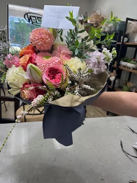 Hand-tied bouquet of pink, peach, and white flowers wrapped in dark paper