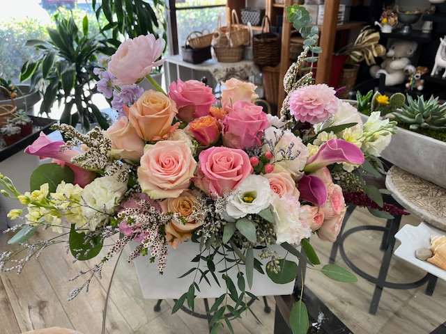 Mixed pastel bouquet with roses, calla lilies, and other blooms in a white container