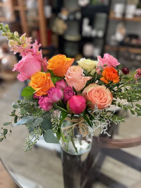 Mixed bouquet of pink, orange, and peach roses in a glass vase