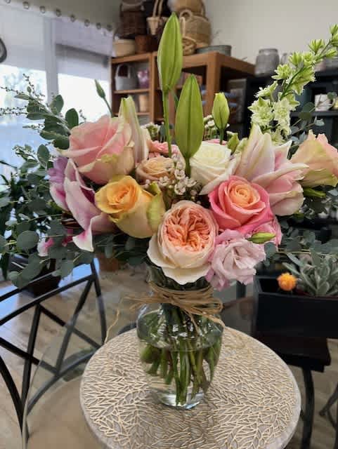 Mixed bouquet of pink roses, lilies, and white blooms in a glass vase