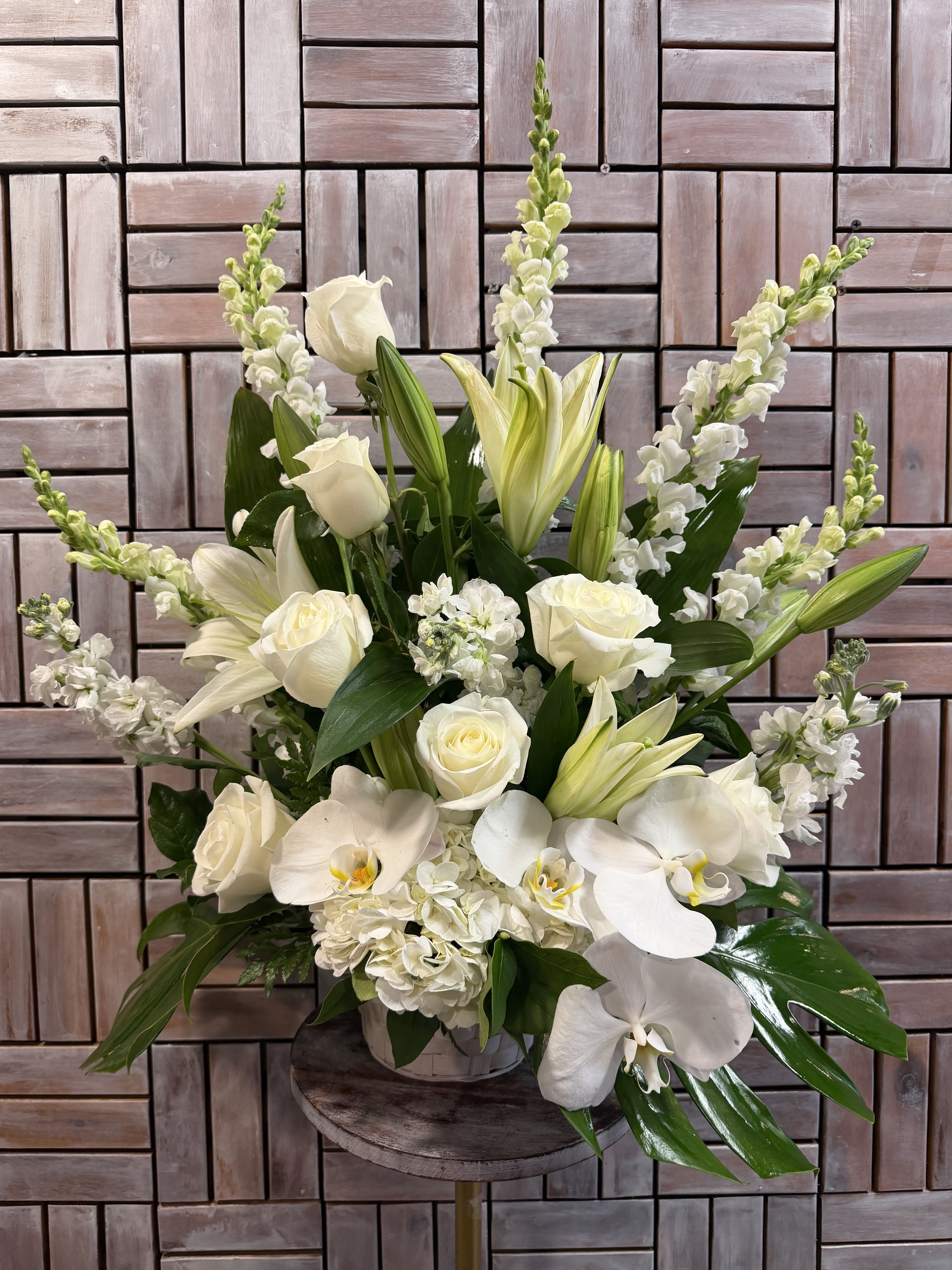 Hope by Unique K Floral Studio - An all-white funeral basket featuring lilies, roses, orchids, and more framed by a backdrop of large leaves. Suitable for any type of funeral ceremony 