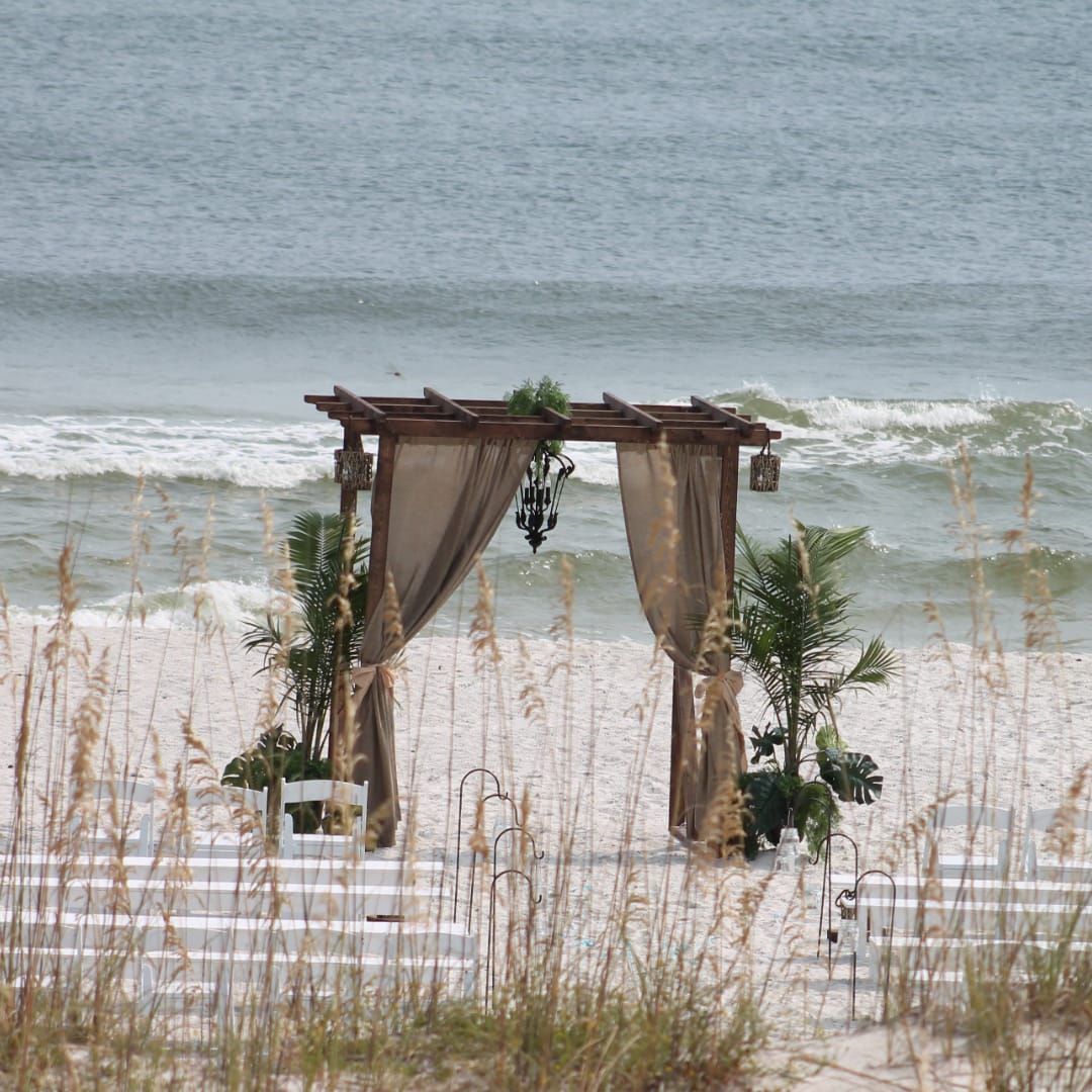 Beach wedding arch with draped curtains and chairs on the sand