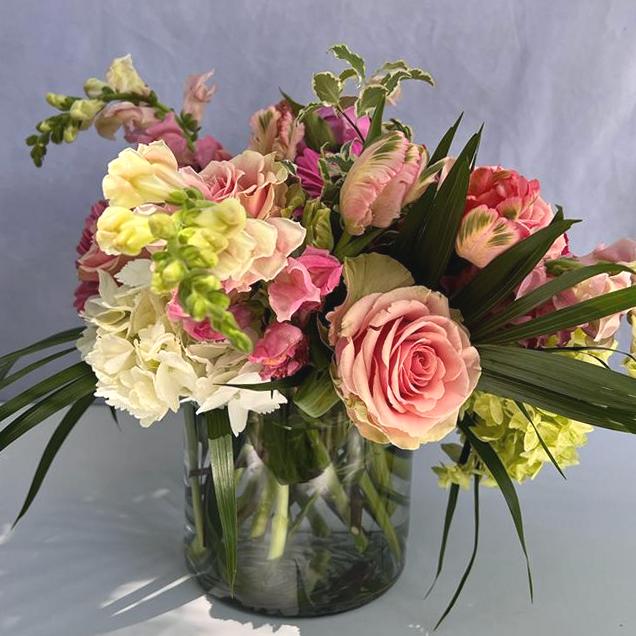 Pastel pink and yellow arrangement with roses, snapdragons, and hydrangeas in a clear glass vase