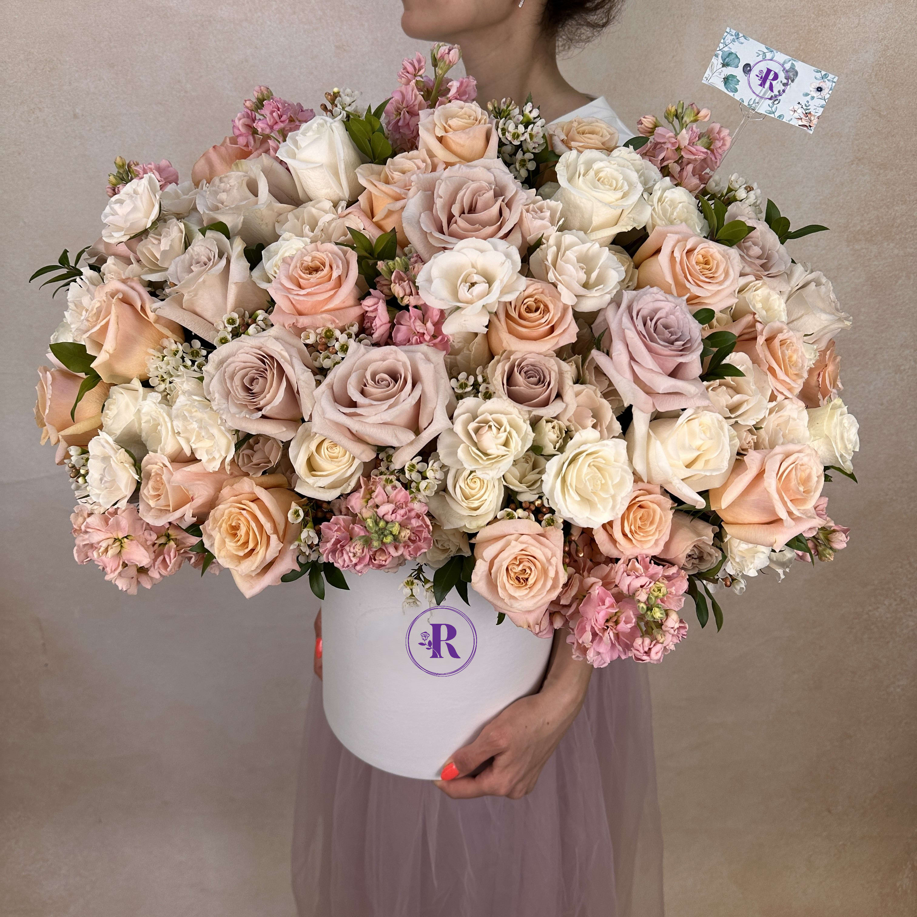 Large hatbox arrangement of cream, blush, and peach roses with pink filler flowers.