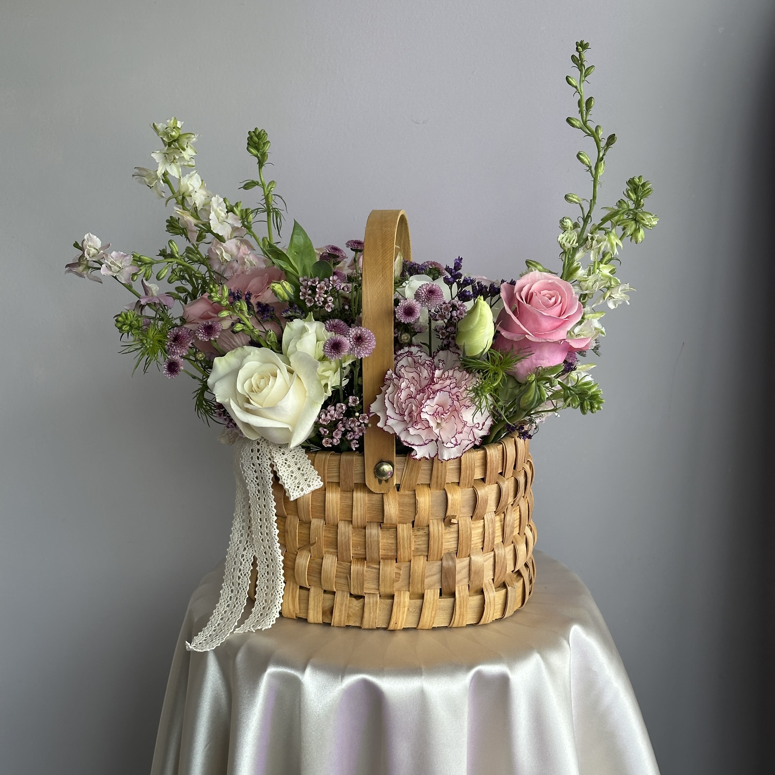Pastel pink and white flower arrangement in a woven basket on a draped table.