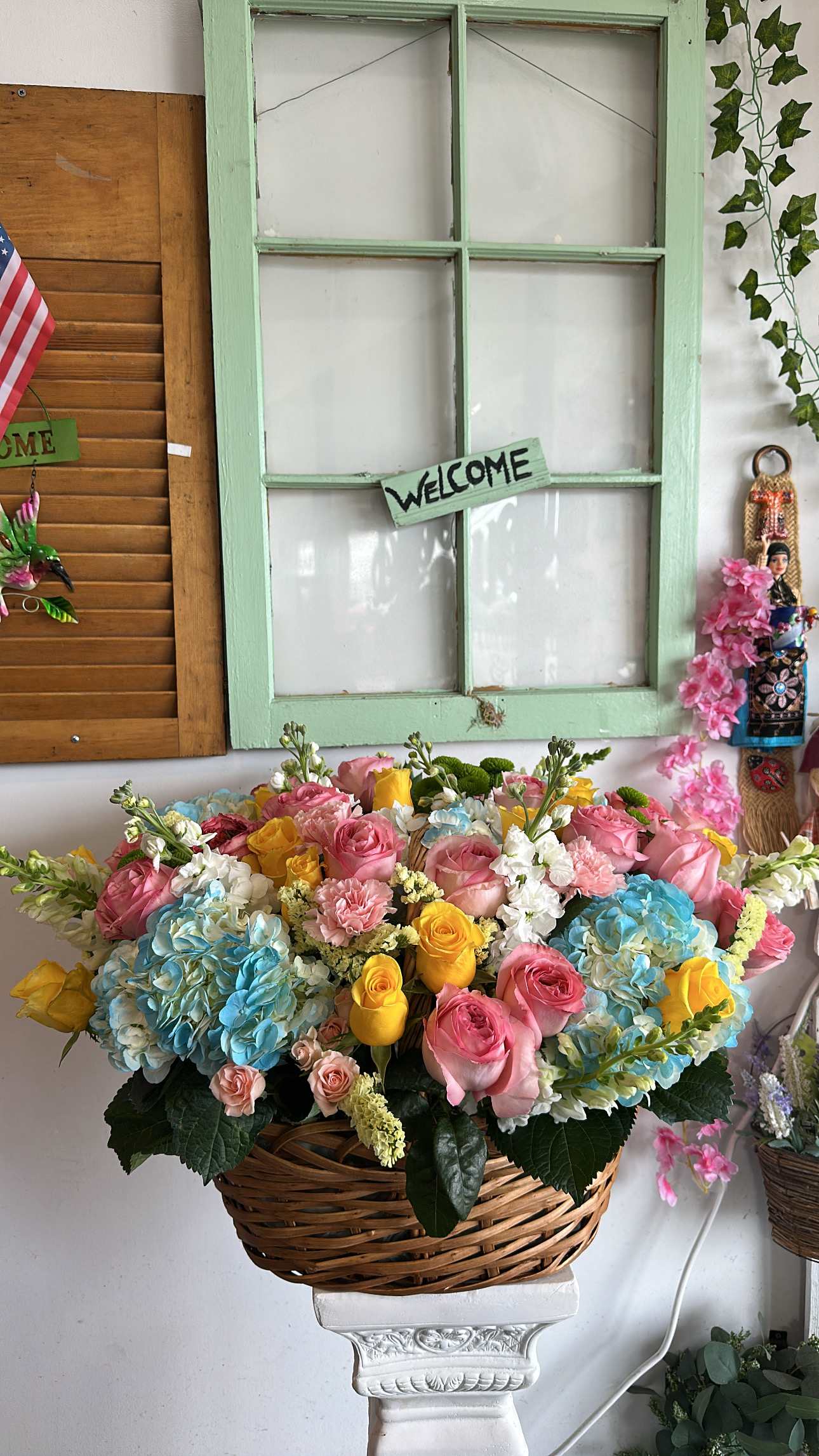 Basket arrangement of pink, yellow, and blue flowers on a pedestal