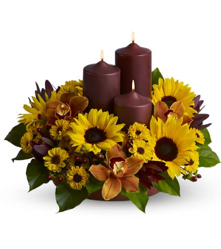 Rustic Radiance  - This rustic display of three chocolate-colored pillar candles surrounded by bright sunflowers, orchids and more, in glowing tones of yellow and bronze, makes a delightful centerpiece for a Thanksgiving feast or fall dinner party, and is also a lovely decorative accent for an entryway.    A mix of fresh flowers such as sunflowers, Viking spray chrysanthemums, cymbidium orchids and more, in shades of yellow and bronze - accented with preserved oak leaves - are arranged in a tray with three chocolate-colored pillar candles of different heights.    Approximately 18" (W) x 13" (H)    Orientation: All-Around        As Shown : TFWEB459    
