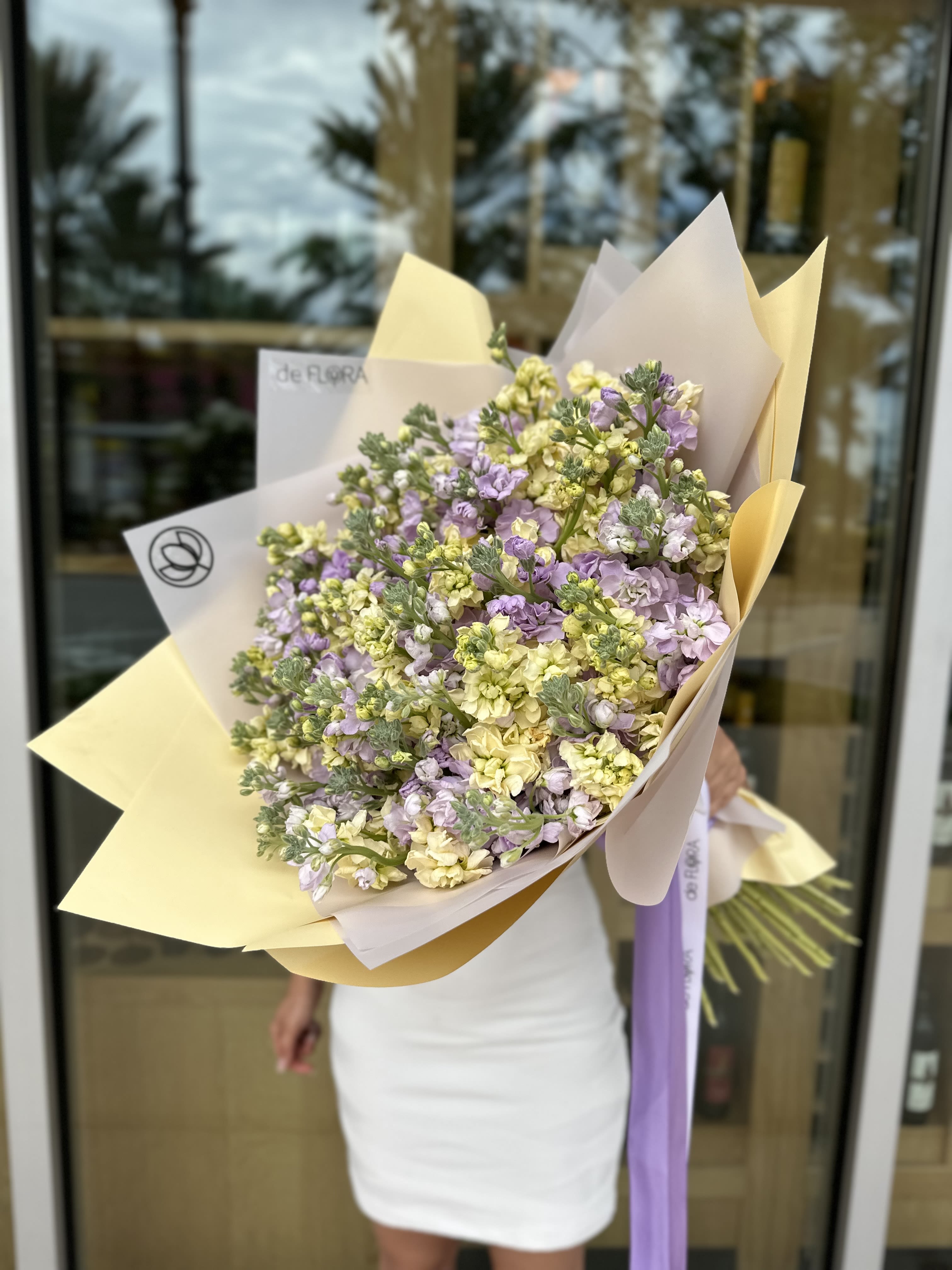 Large bouquet of pale yellow and lavender flowers wrapped in cream paper