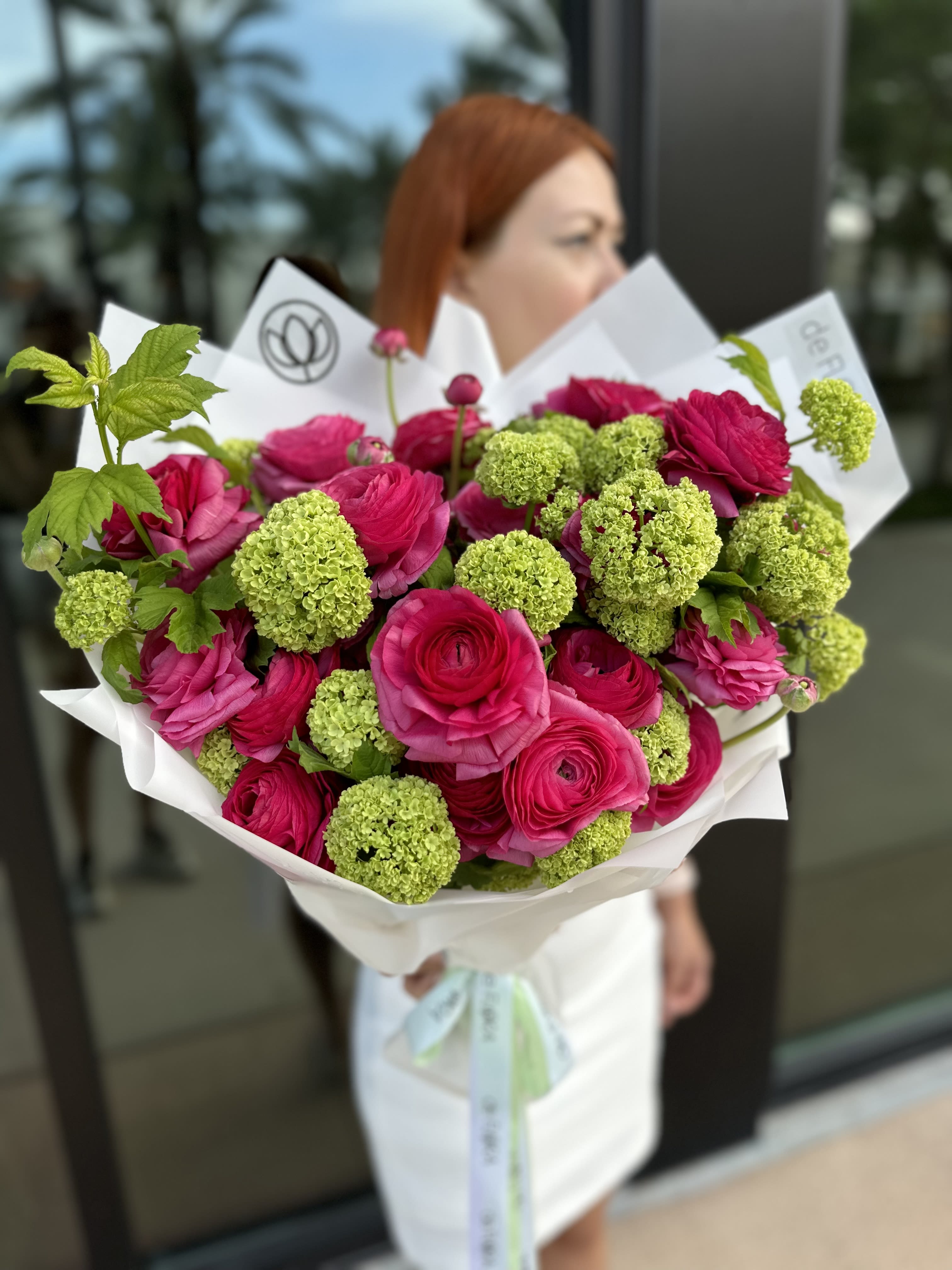 Bouquet of hot pink roses and green pom-pom blooms wrapped in white paper