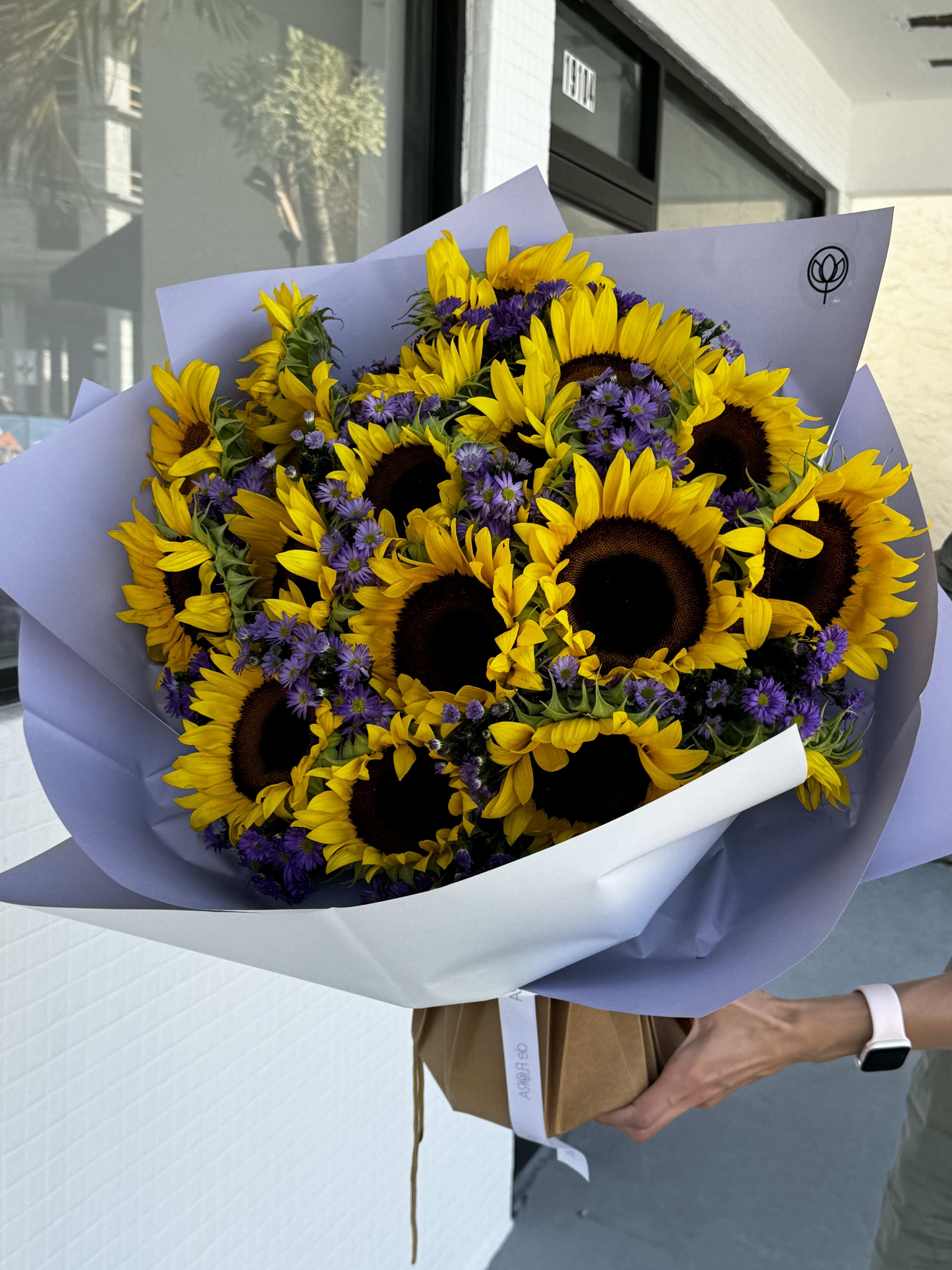 Bouquet of sunflowers and purple daisies wrapped in lavender paper