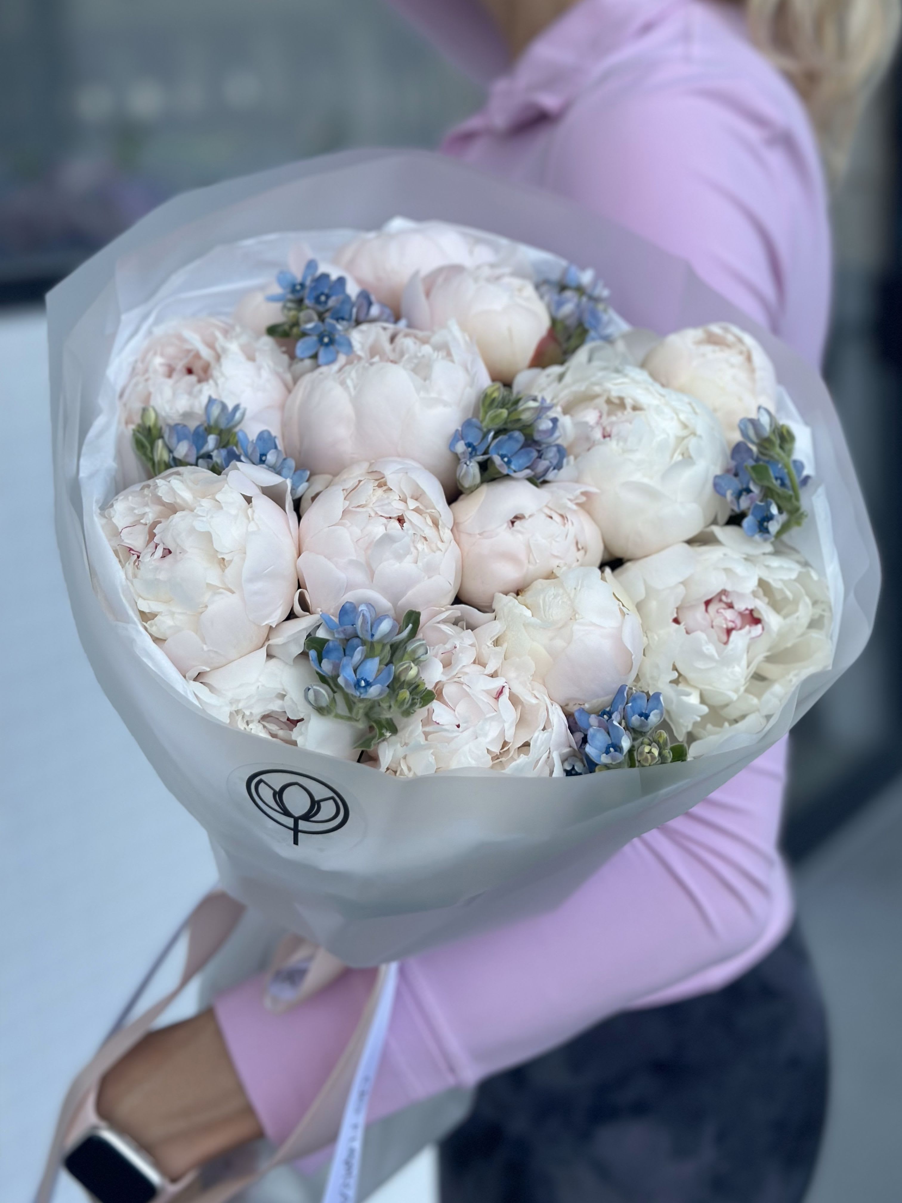 Bouquet of pale pink peonies with small blue flowers wrapped in white paper
