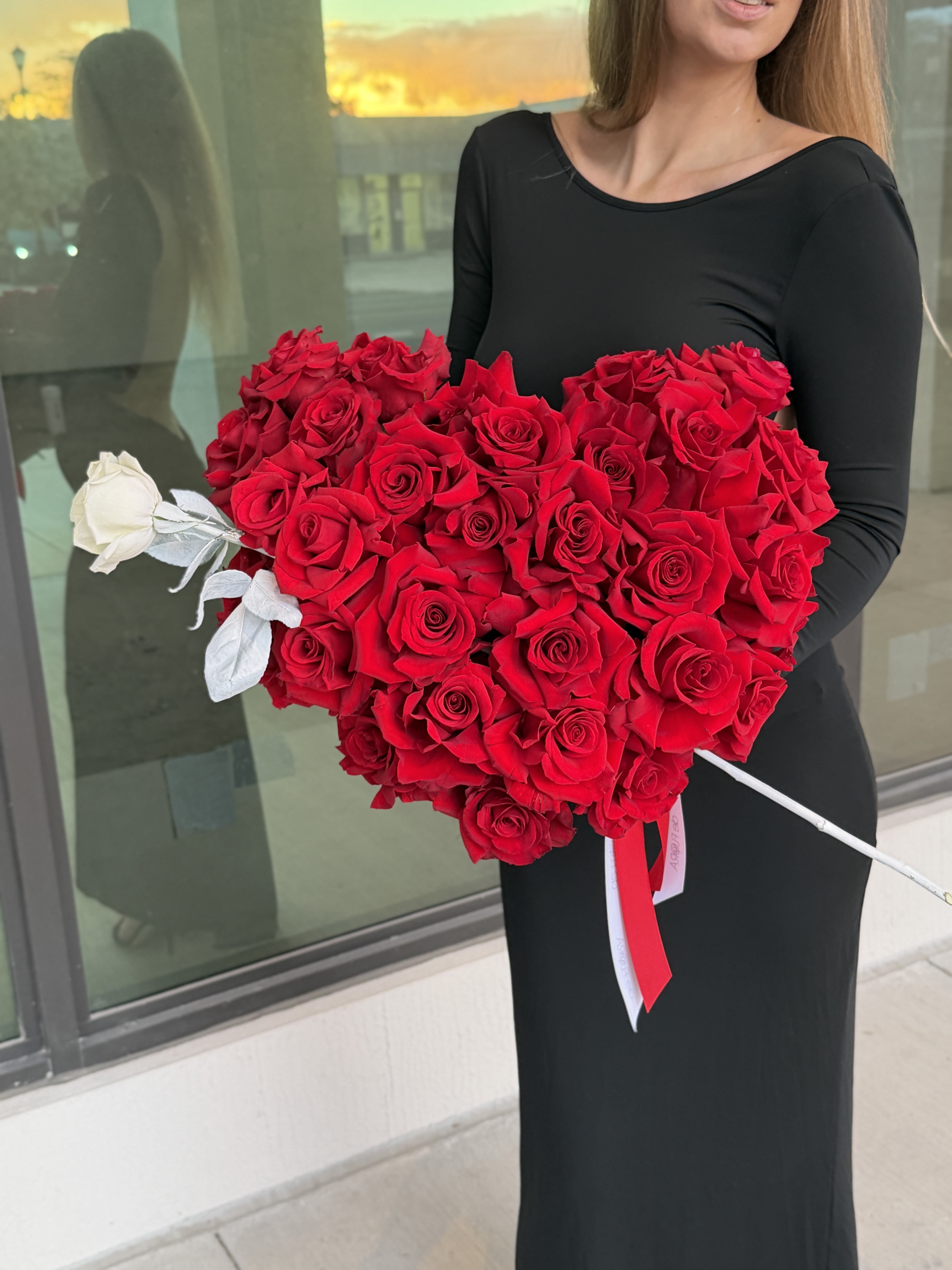 Heart-shaped bouquet of red roses with a single white rose