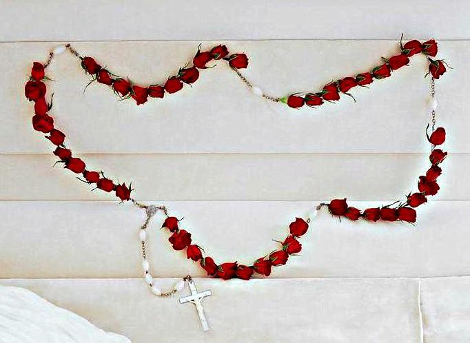 Red rose garland draped across a light upholstered headboard with a white cross necklace