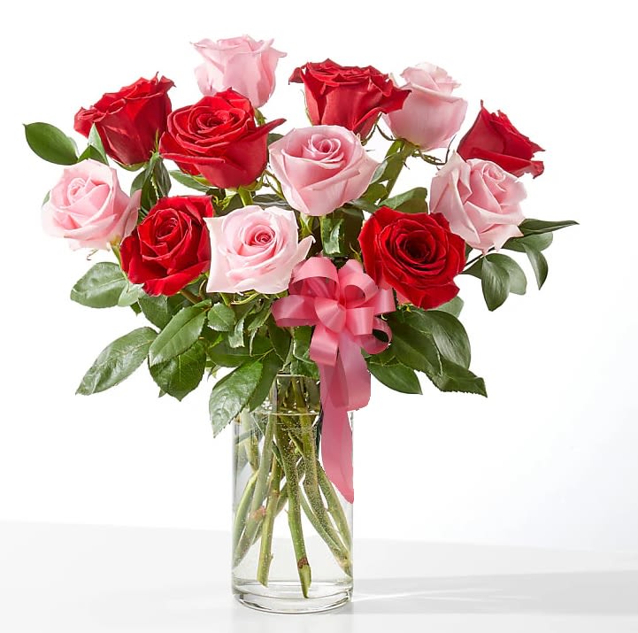 Bouquet of red and pink roses in a clear glass vase with a pink ribbon