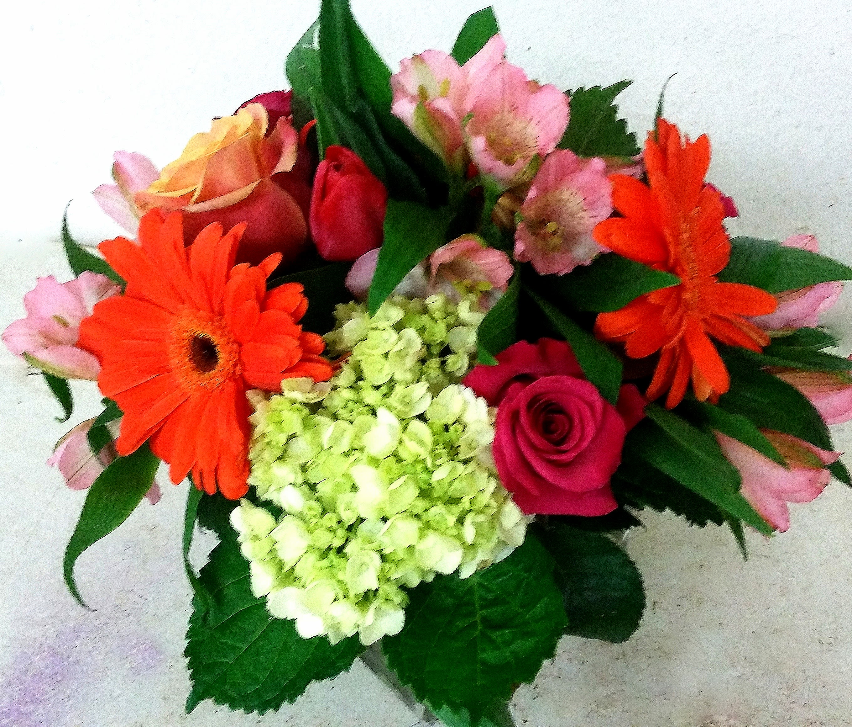 Bouquet of orange gerbera daisies, pink roses, and pale green hydrangea