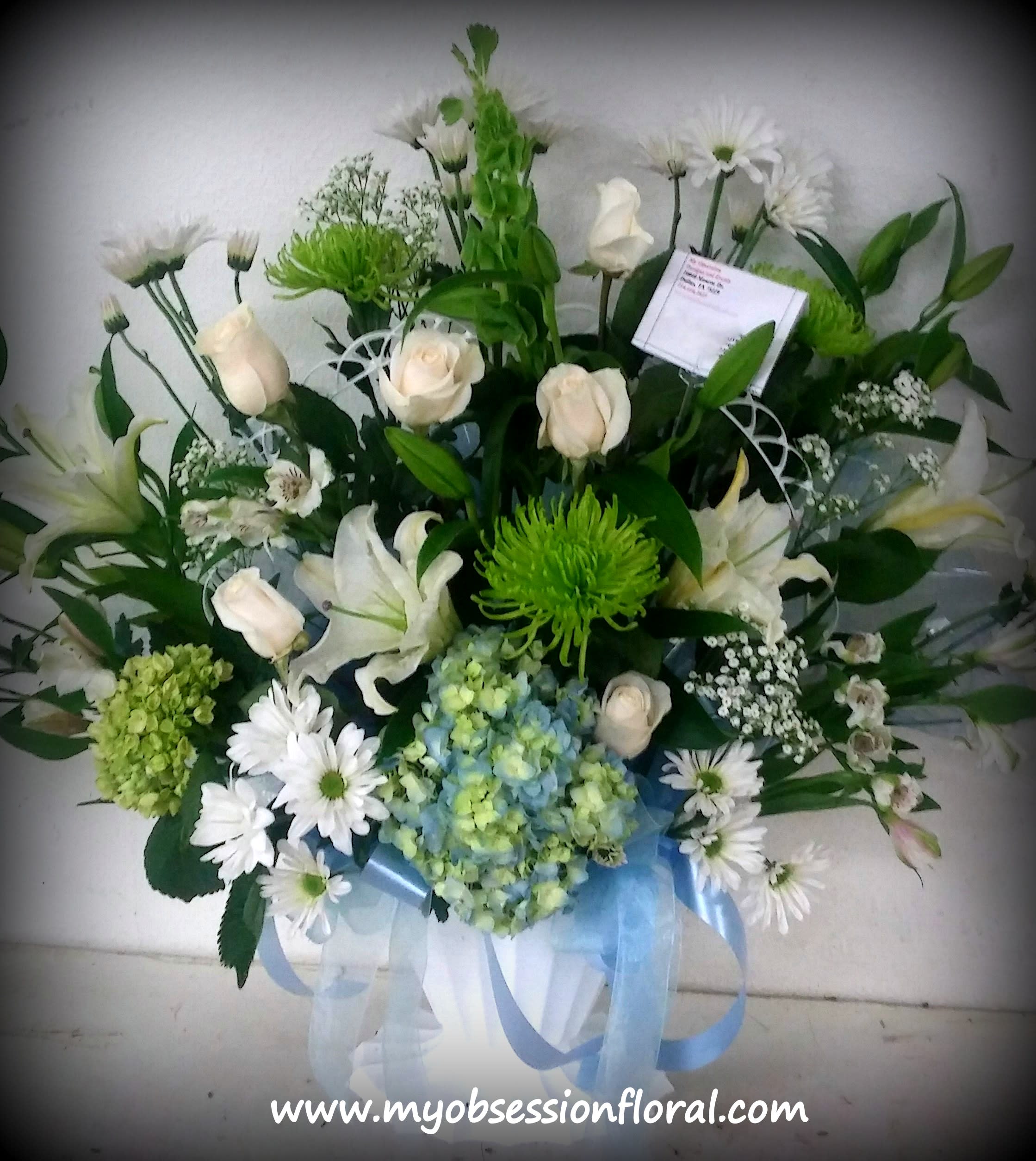 White roses and lilies with green and blue flowers in a ribboned bouquet