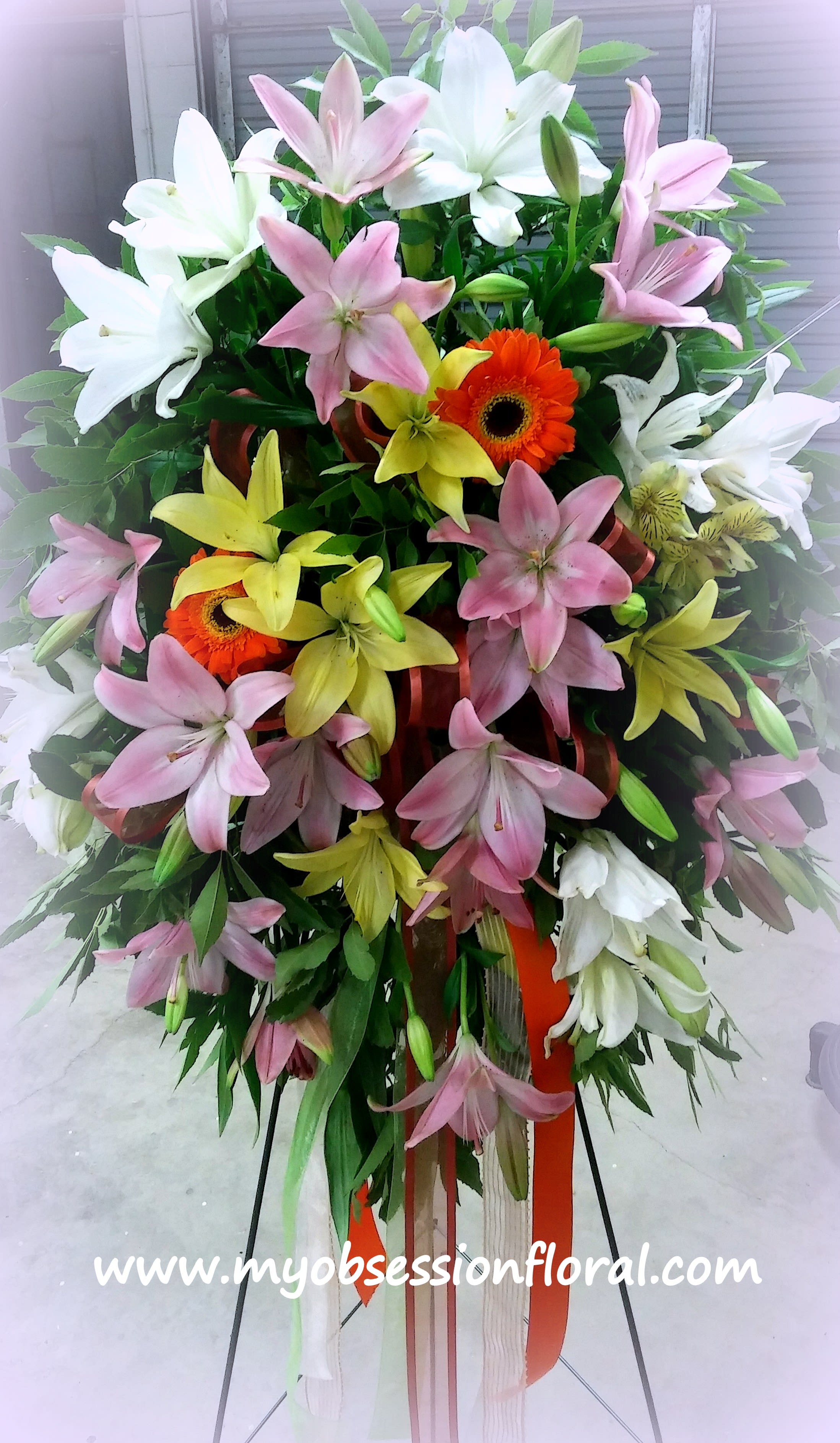 Tall standing spray of lilies and gerbera daisies in pink, white, and yellow
