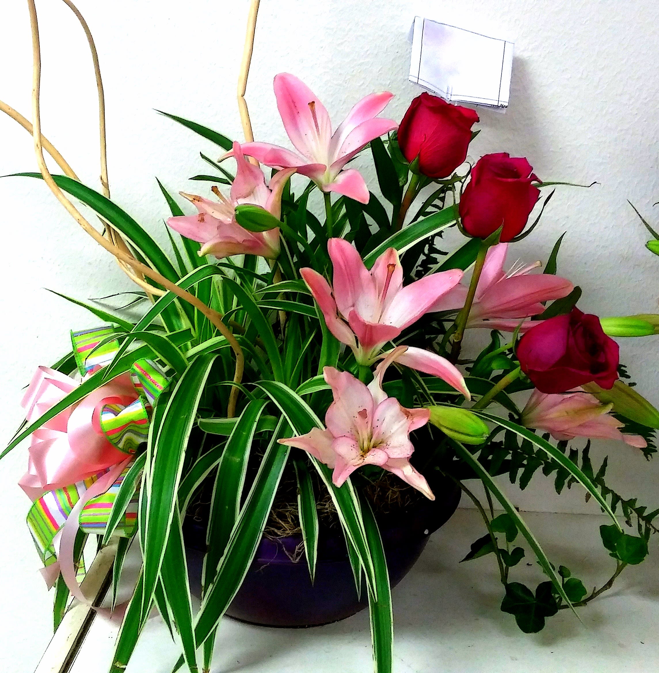 Pink lilies and red roses in a dark vase with a ribbon bow