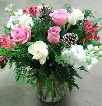Pink and white roses arranged in a glass vase with greenery and a pinecone