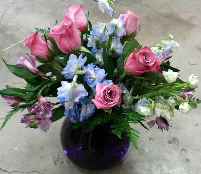 Pink roses and blue flowers arranged in a dark glass vase