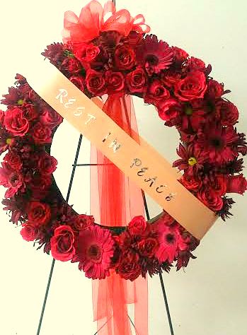 Red floral wreath with a peach ribbon on a stand
