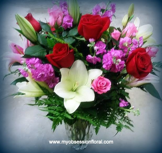 Bouquet of red roses and white lilies with pink filler flowers in a glass vase