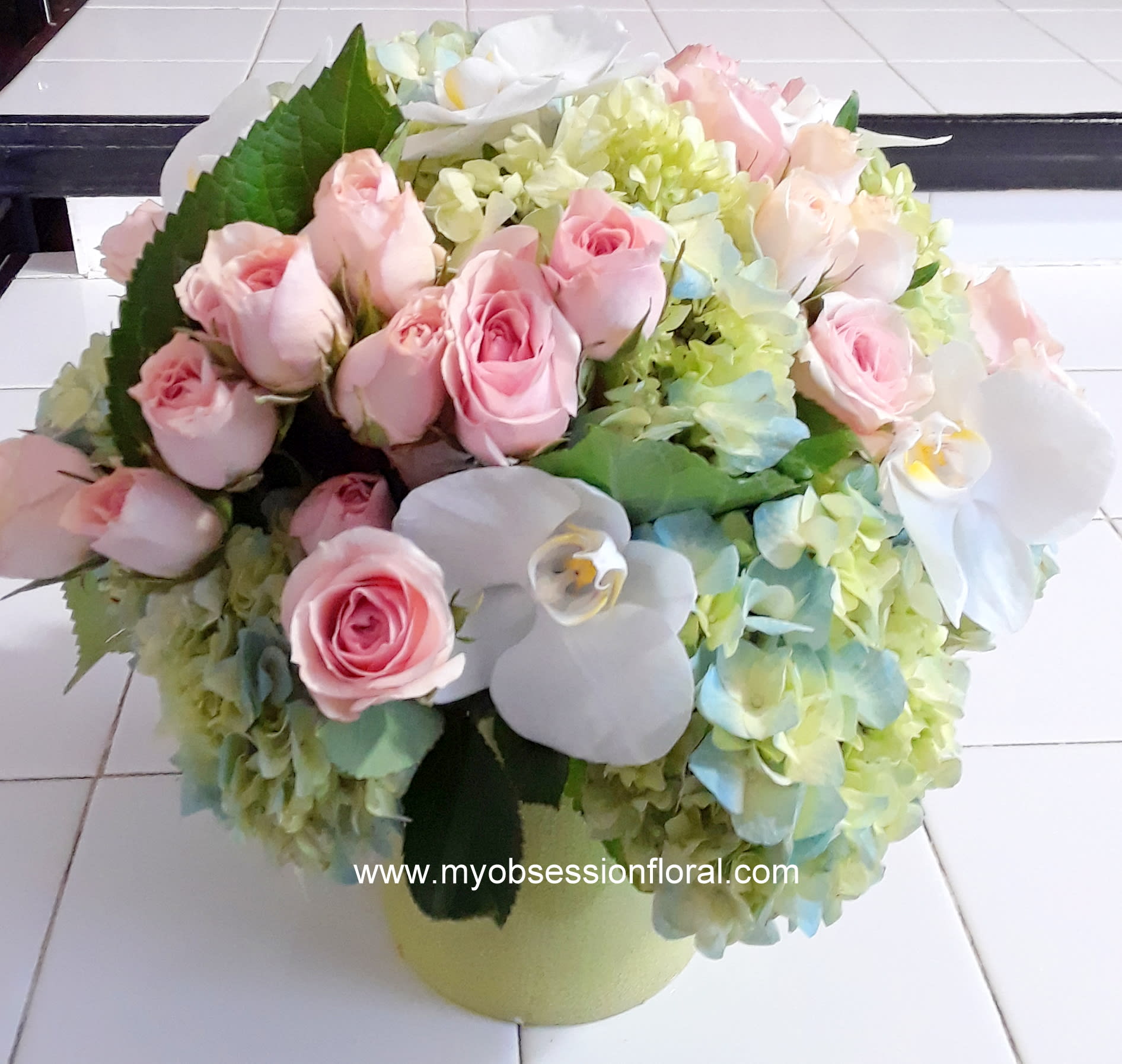 Pink roses and white orchids arranged with pale hydrangeas in a round vase