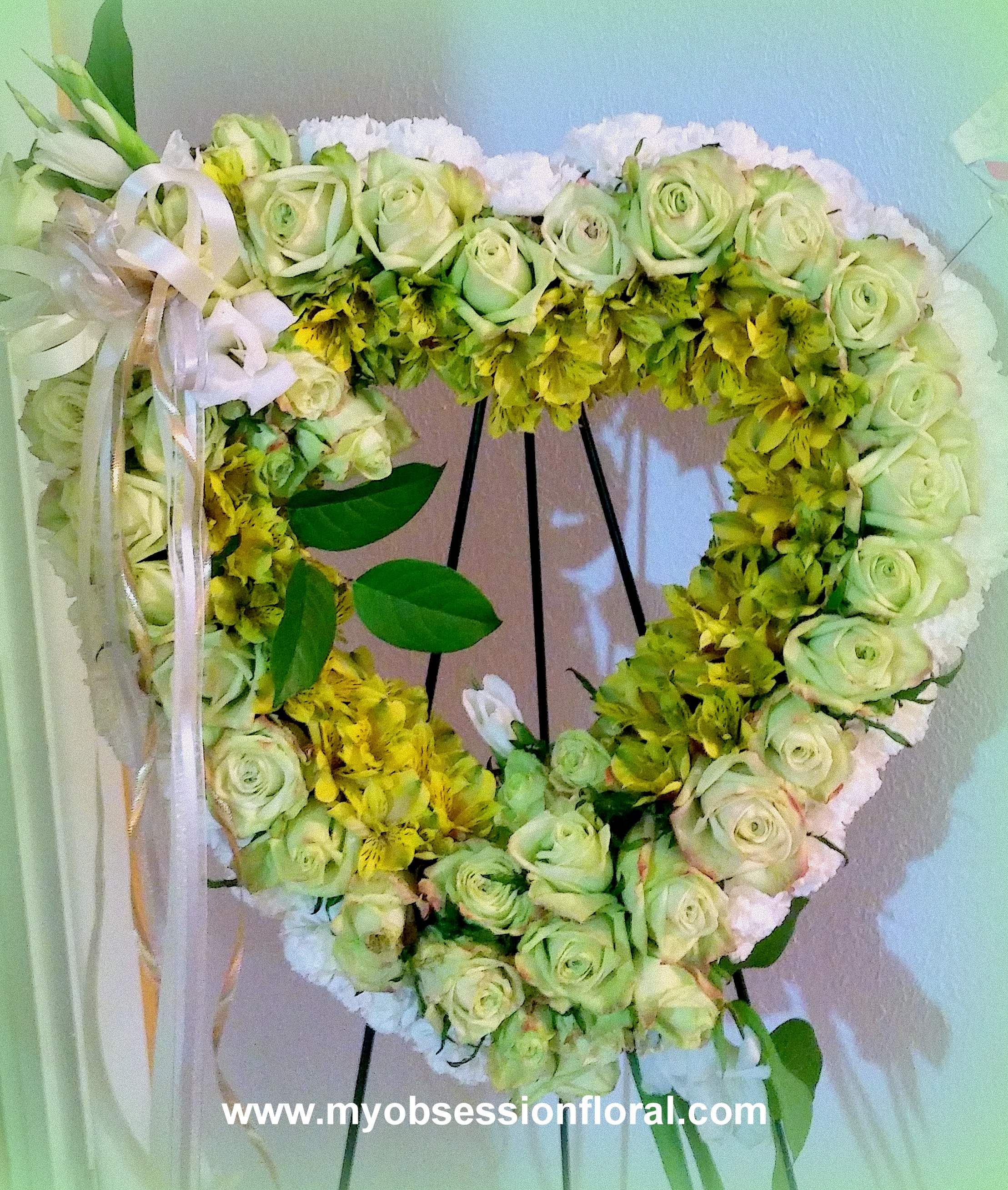 Heart-shaped floral wreath with pale green roses and yellow flowers on a stand