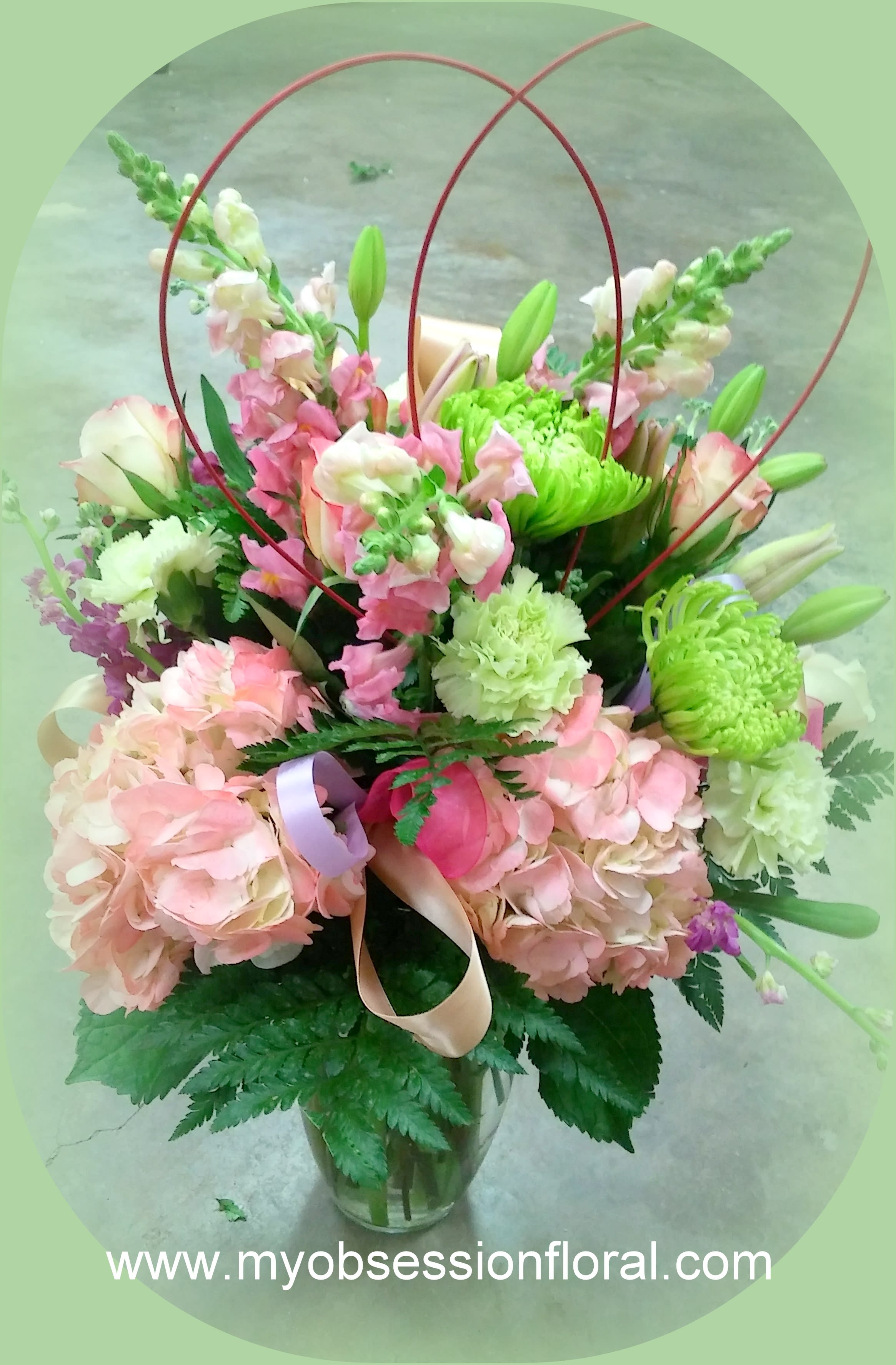 Pink and green mixed bouquet in a glass vase with ribbon loops