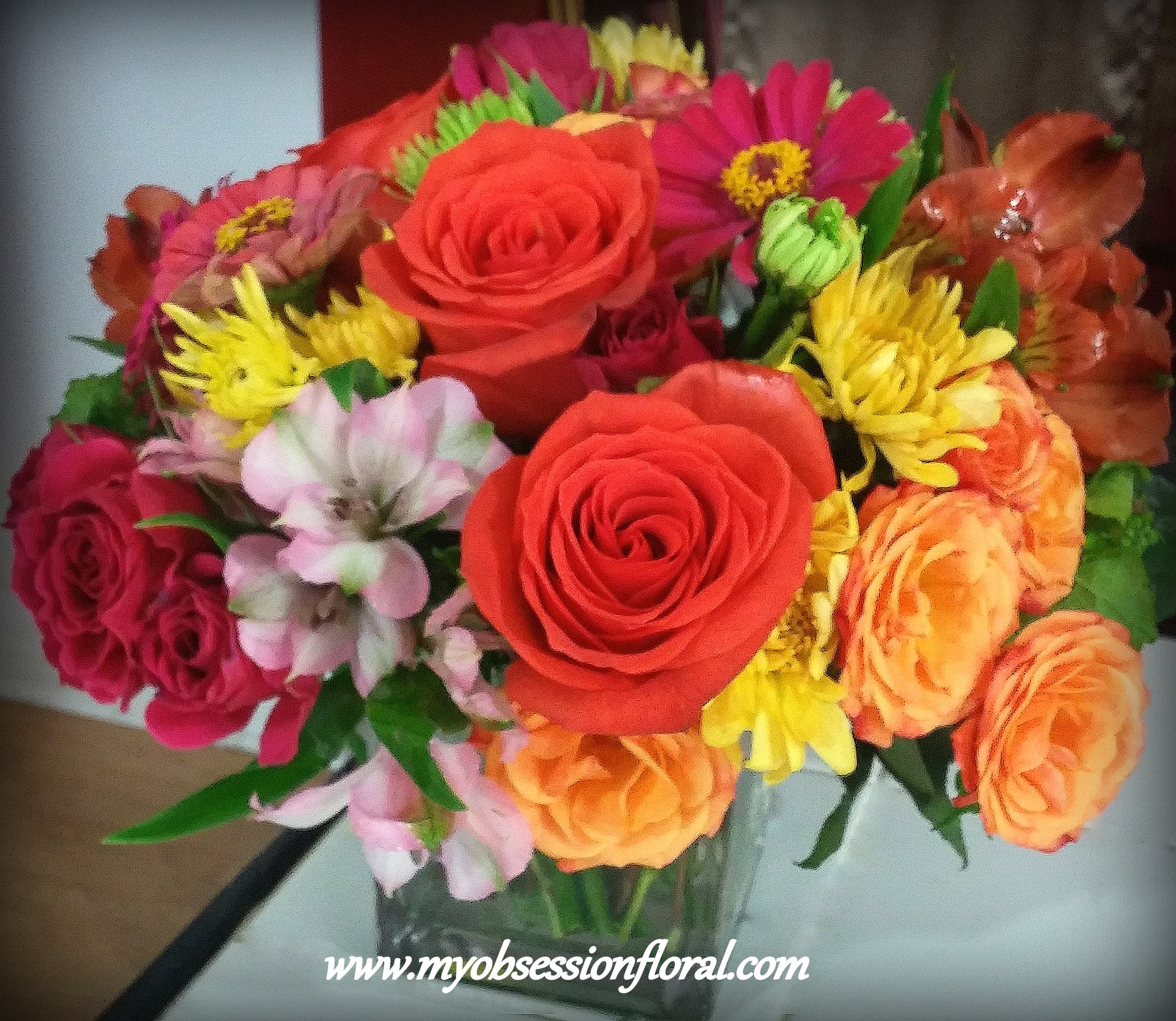 Mixed bouquet of roses, daisies, and orange blooms in a glass vase