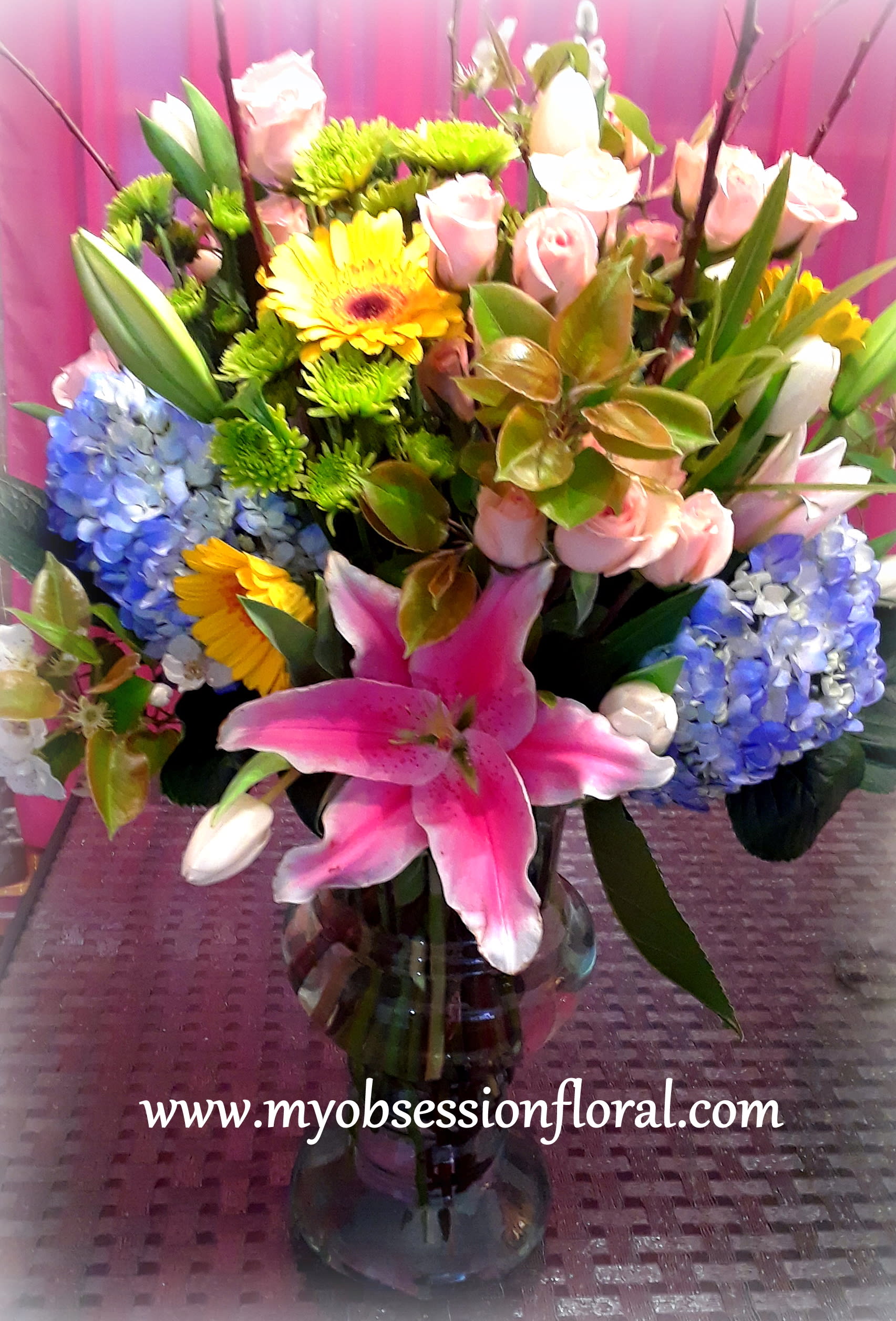 Mixed bouquet in a glass vase with pink lilies, roses, hydrangeas, and yellow daisies