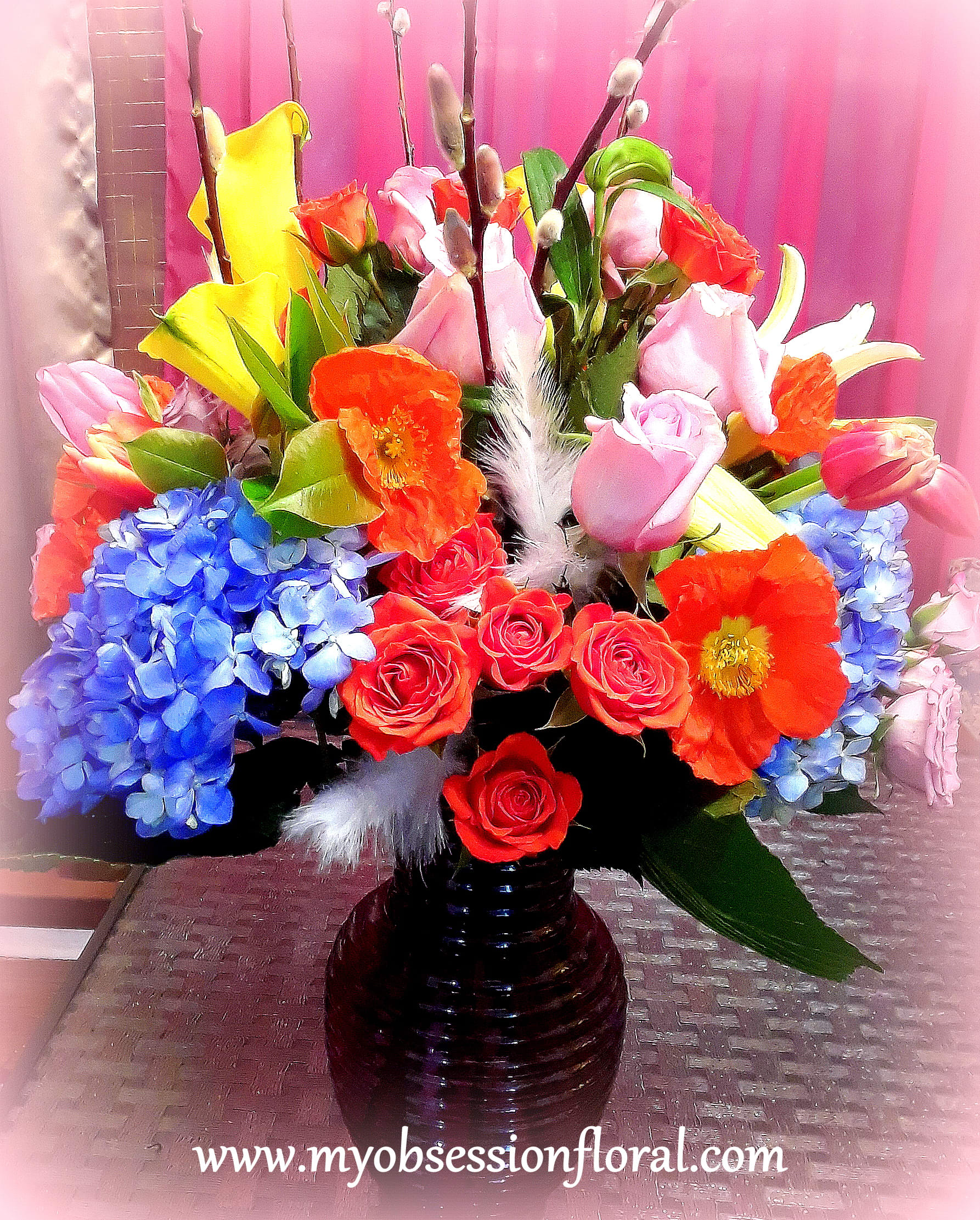 Colorful bouquet of roses, tulips, calla lilies, and hydrangeas in a dark vase