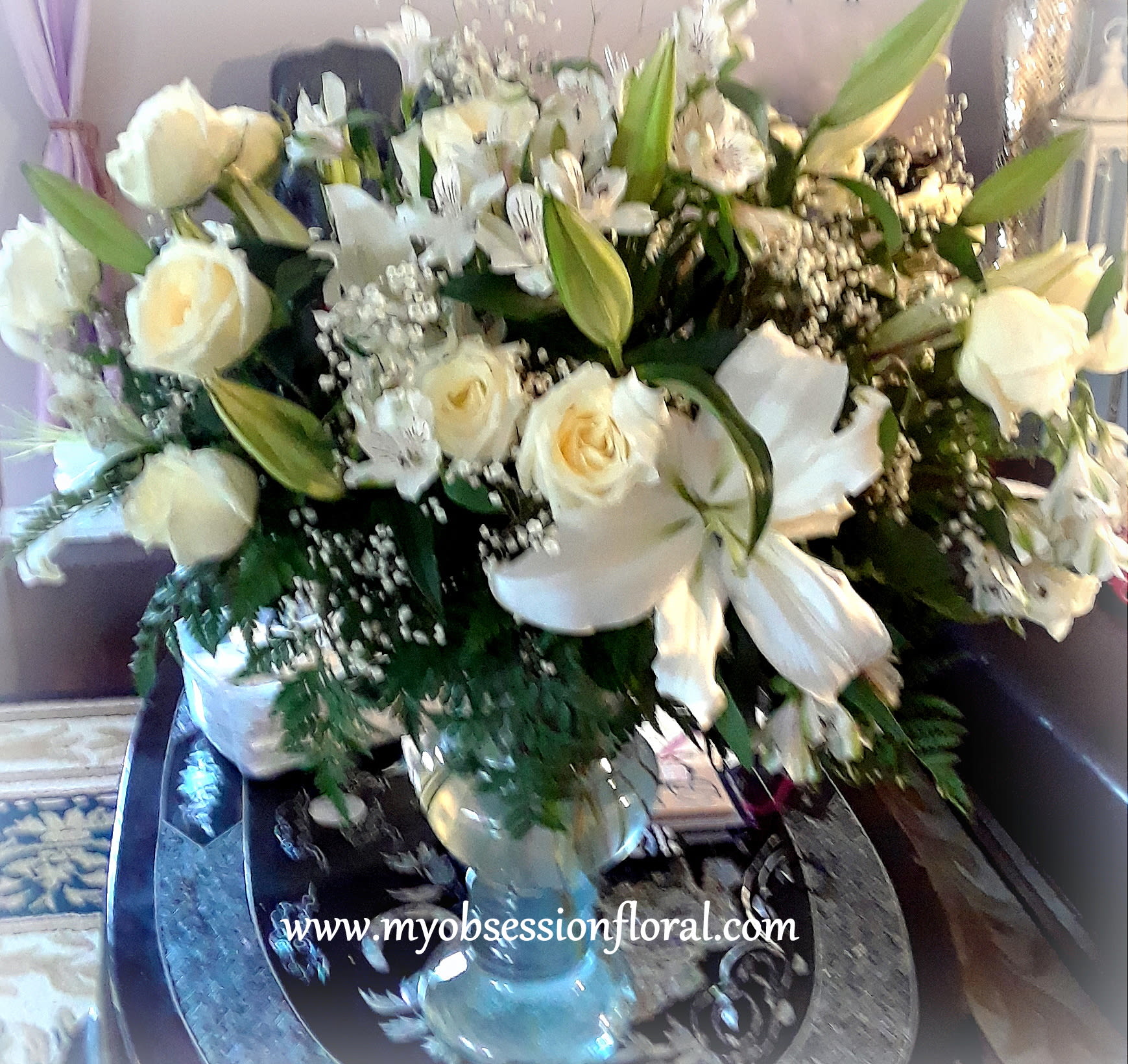 Large white floral arrangement with roses and lilies in a glass vase