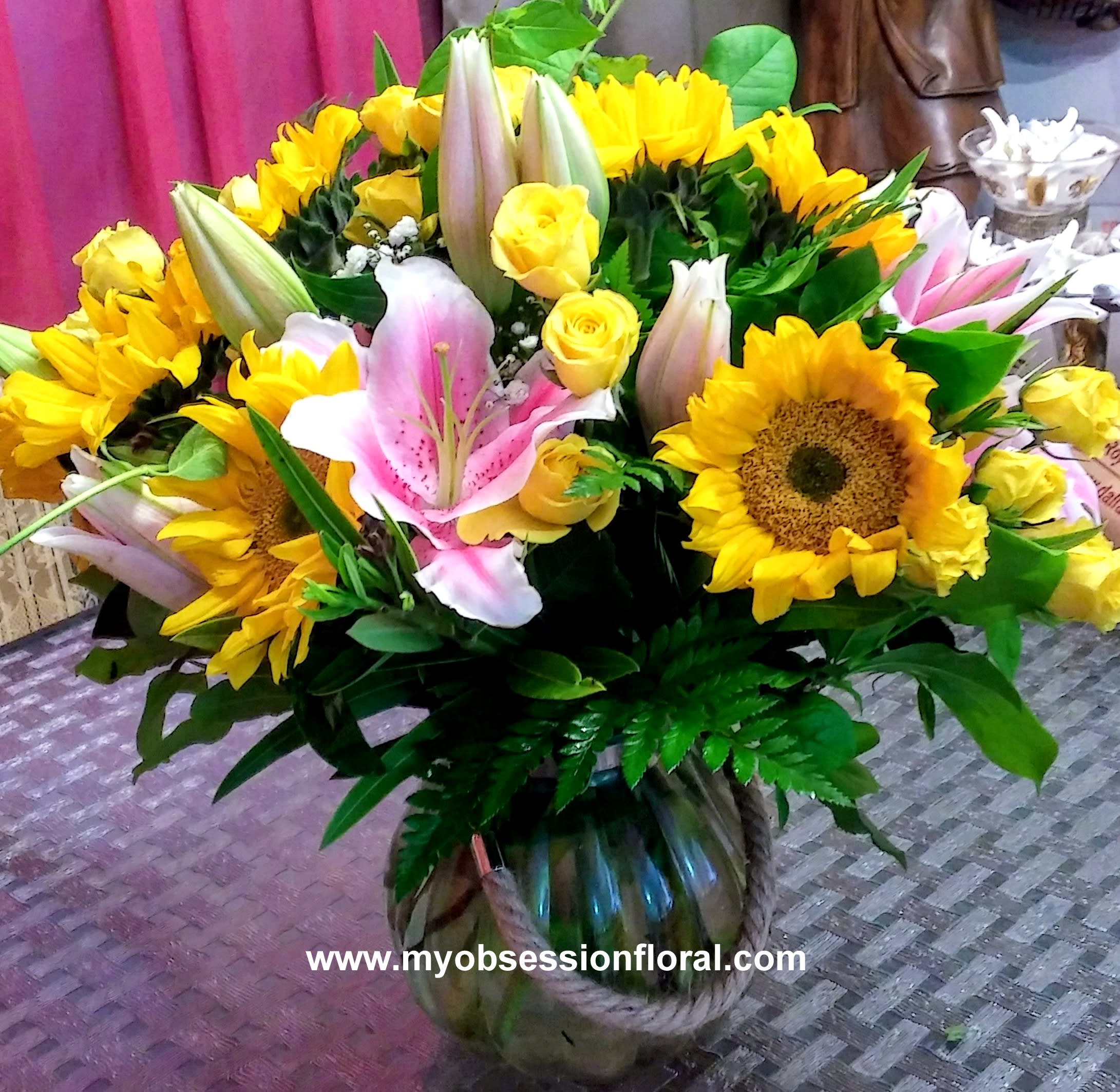 Bouquet of yellow sunflowers, pink lilies, and yellow roses in a glass vase