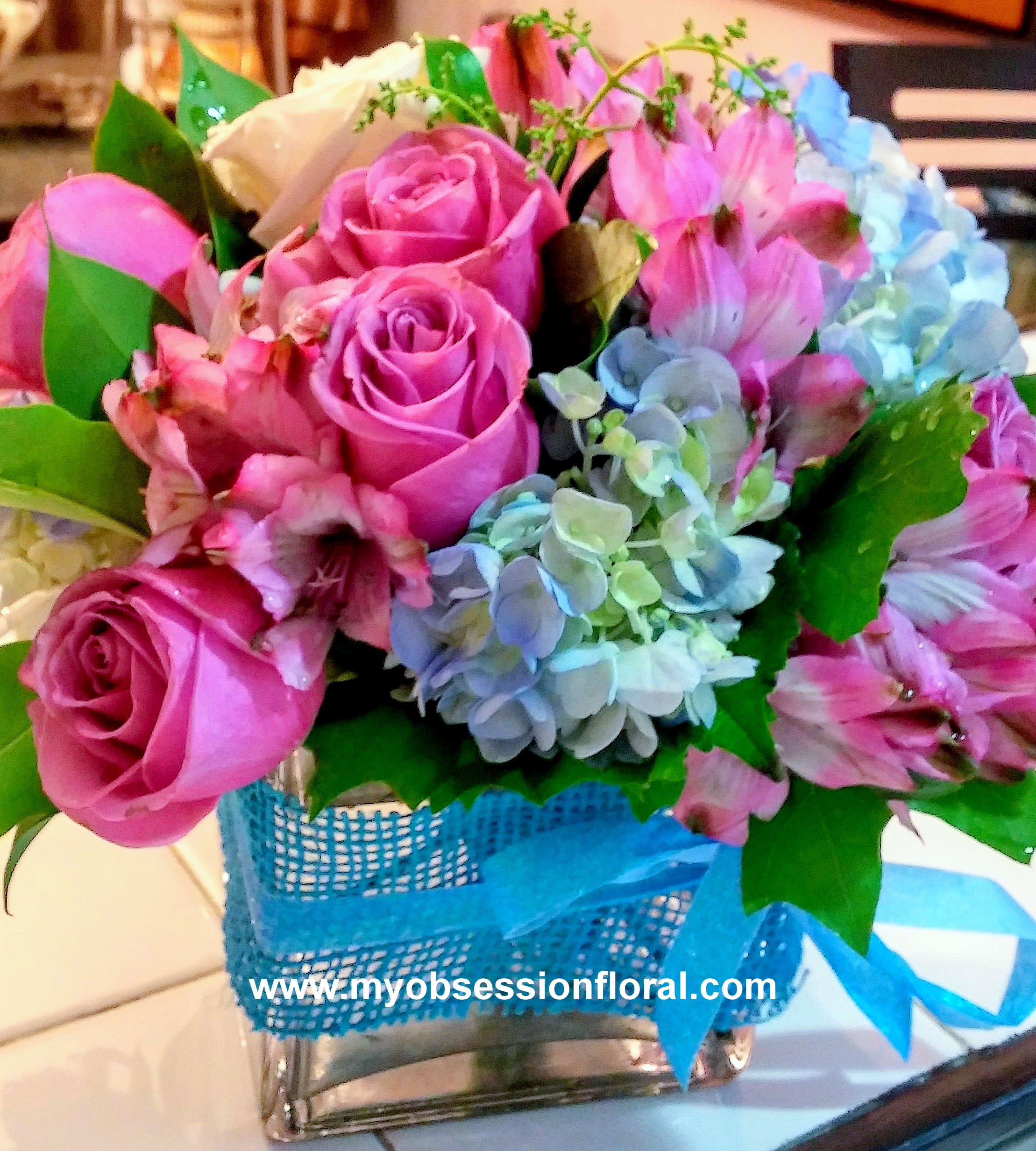 Pink roses and blue hydrangeas in a blue basket with ribbon