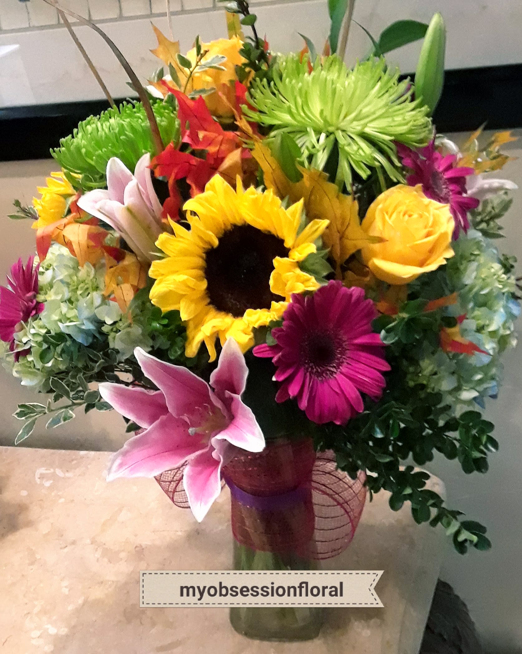 Colorful mixed bouquet in a glass vase with sunflowers, lilies, and chrysanthemums
