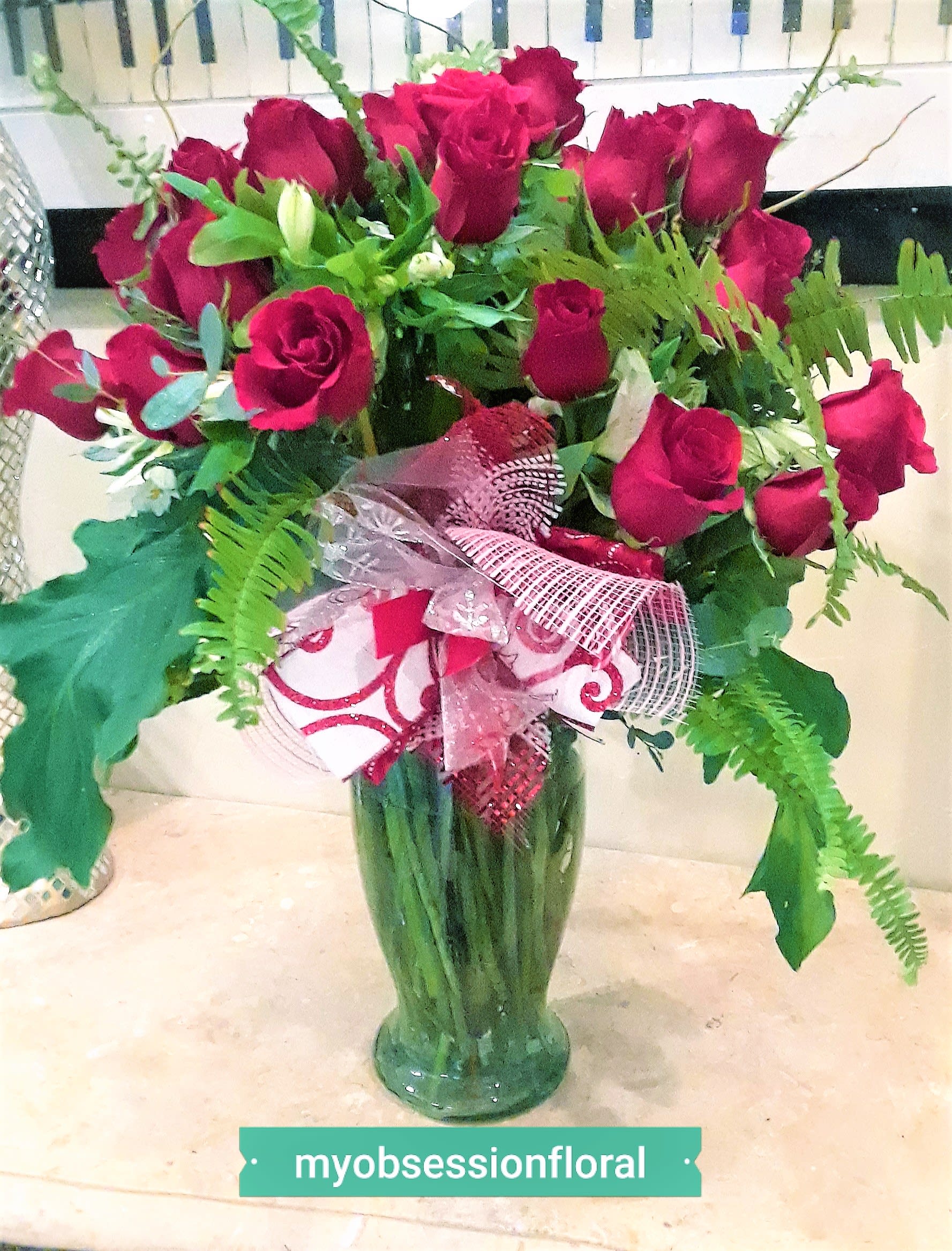 Bouquet of red roses in a green glass vase with a pink ribbon