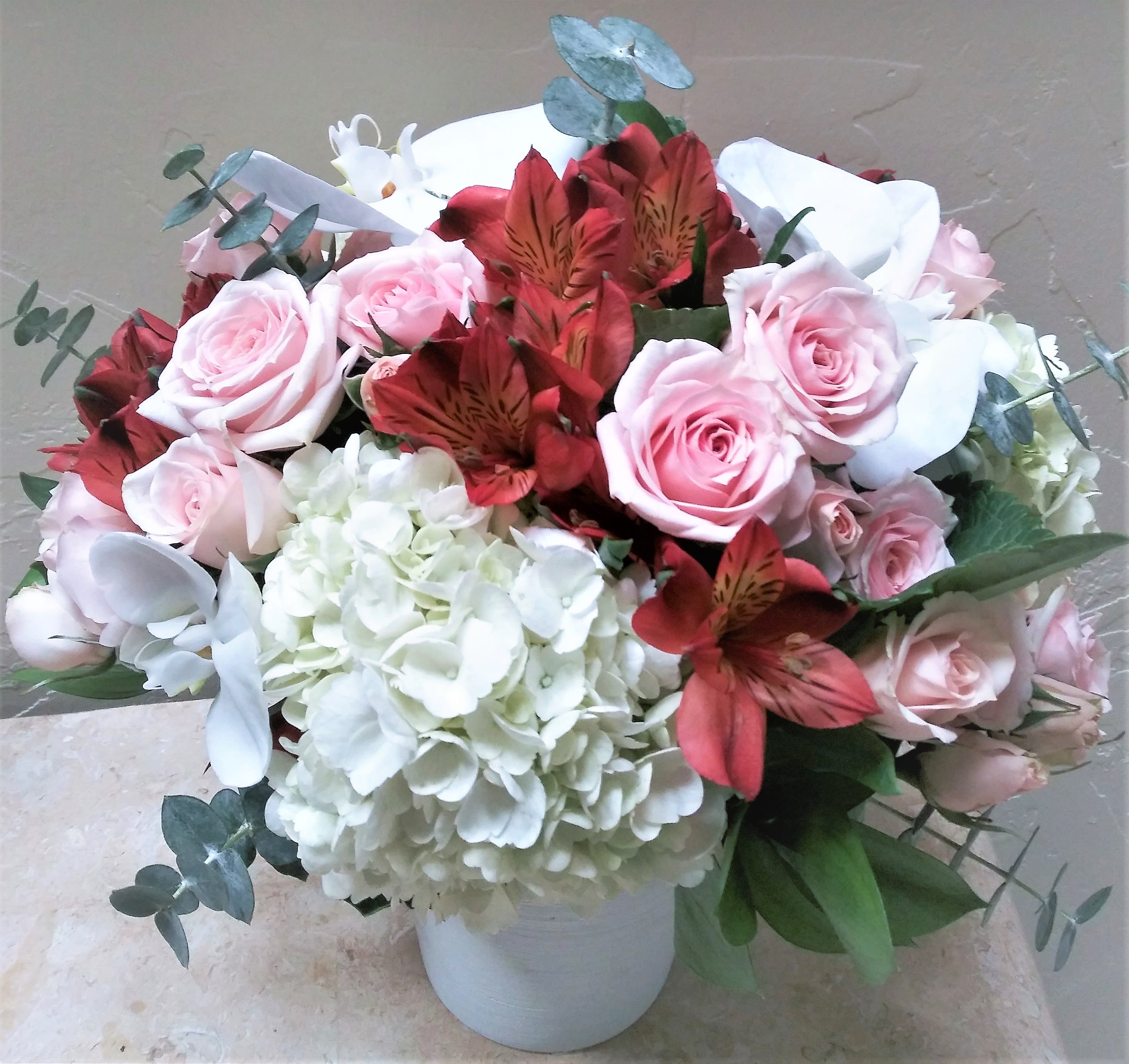 Bouquet of pink roses, white hydrangea, and red alstroemeria in a white vase