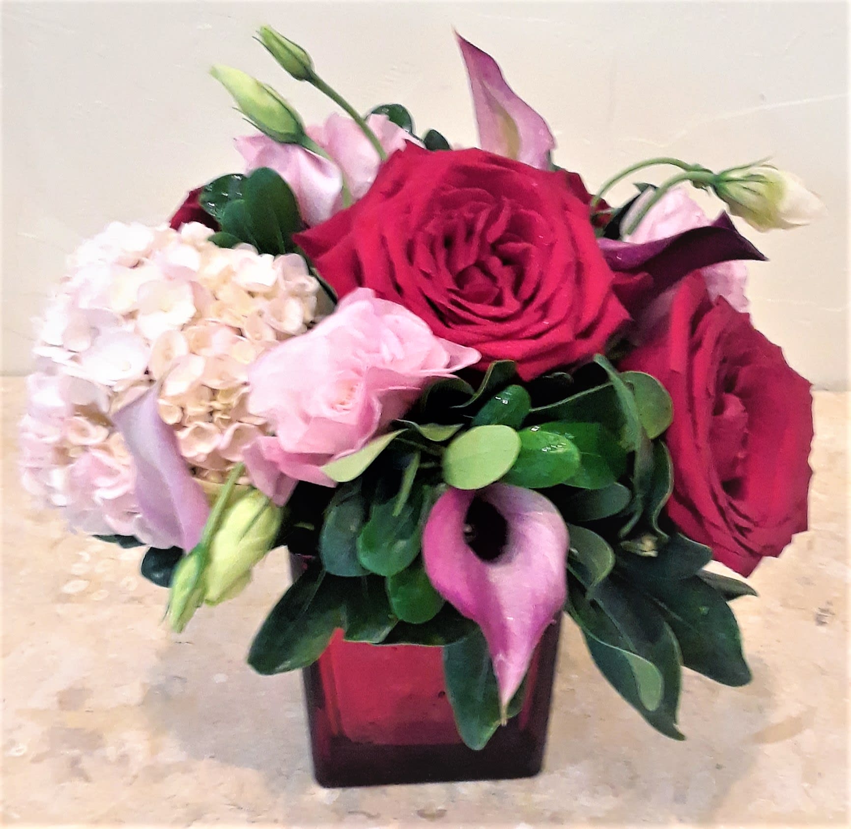 Bouquet of red roses, pink hydrangea, and calla lilies in a square vase