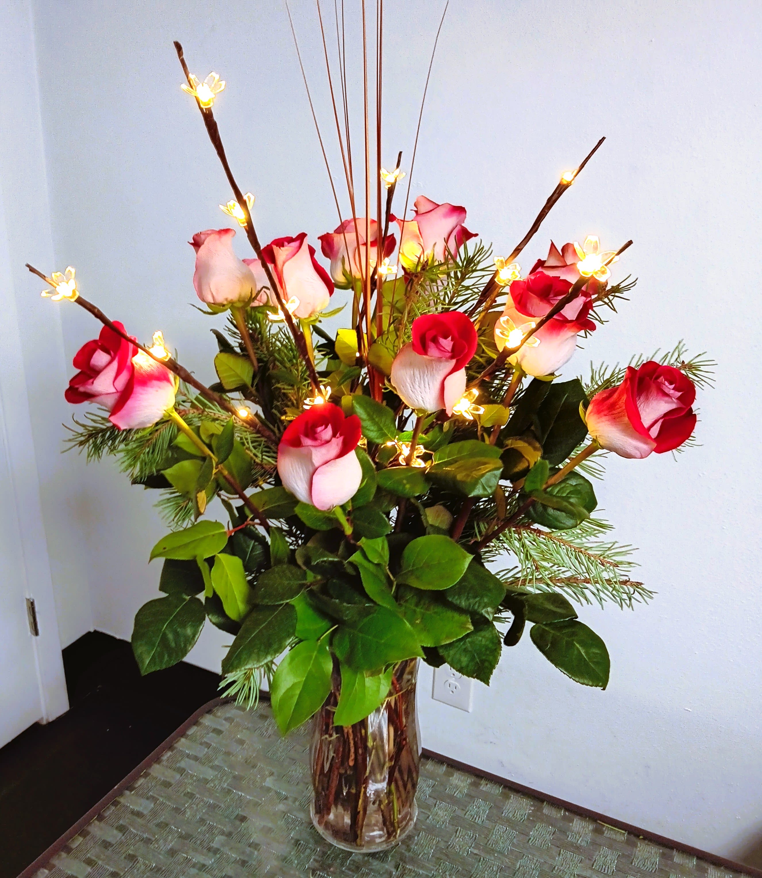 Tall vase arrangement of red and white roses with lit decorative branches