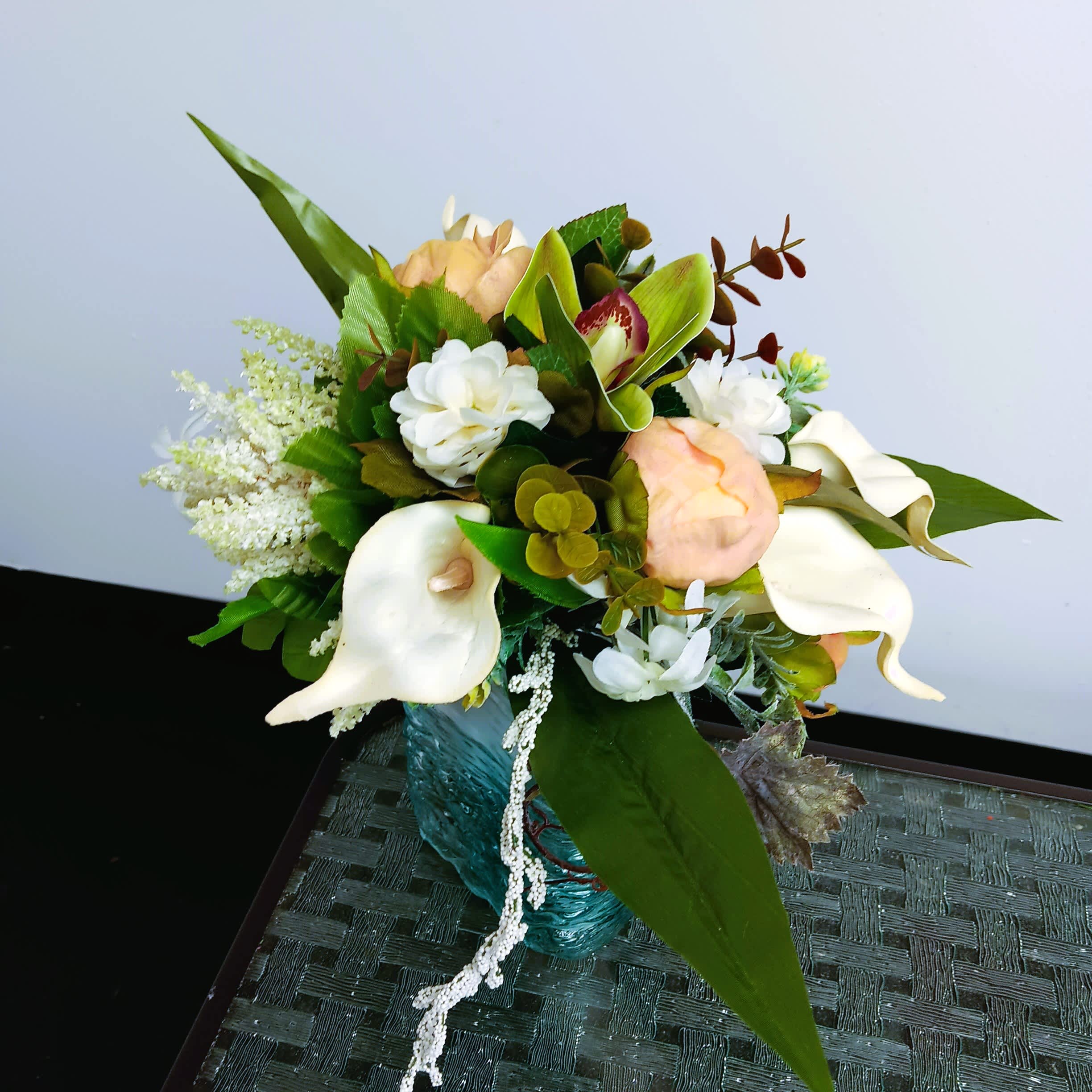 Bouquet with white calla lilies, peach roses, and green foliage in a blue vase.