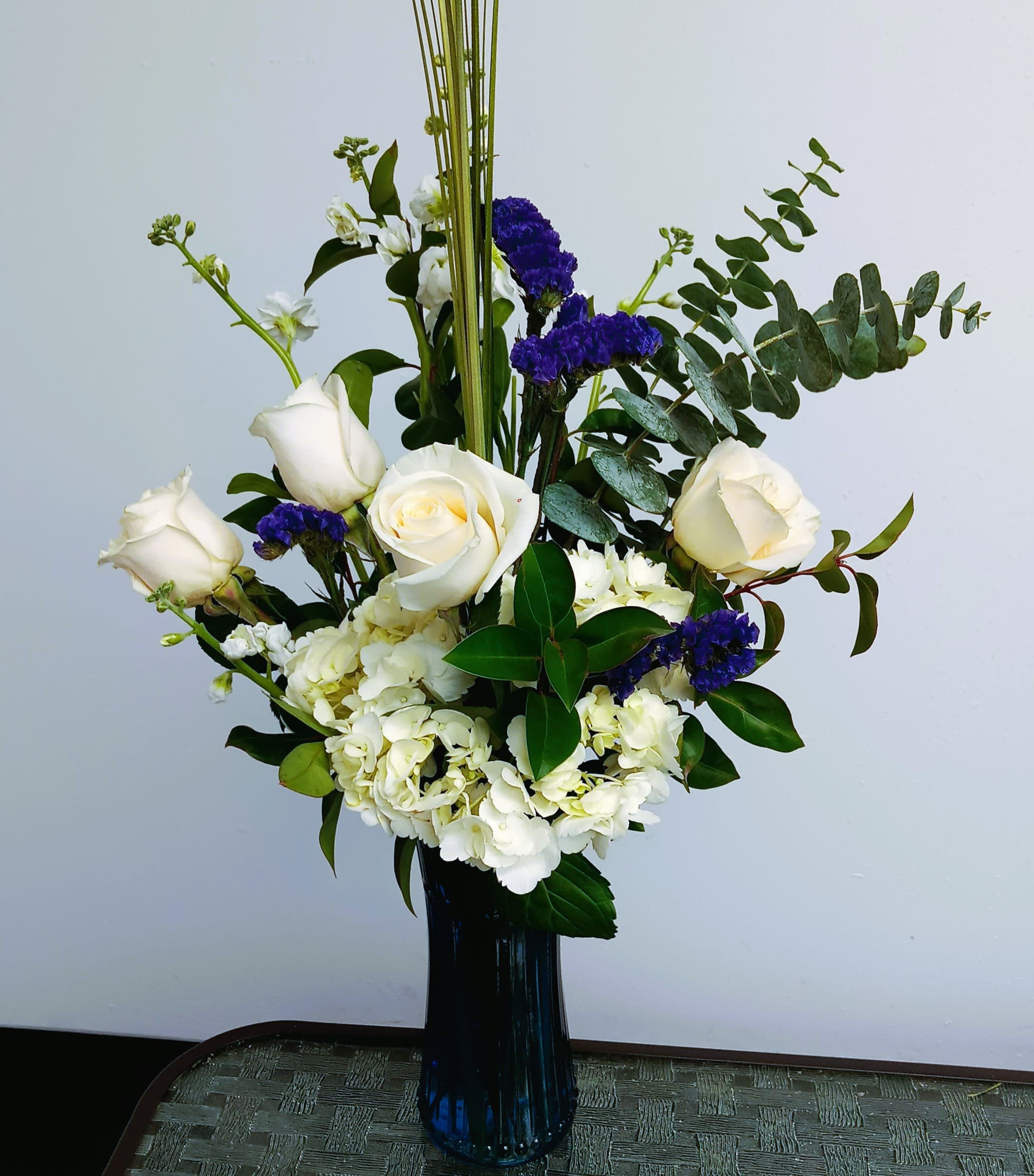 White roses and hydrangeas in a tall blue vase with purple accents