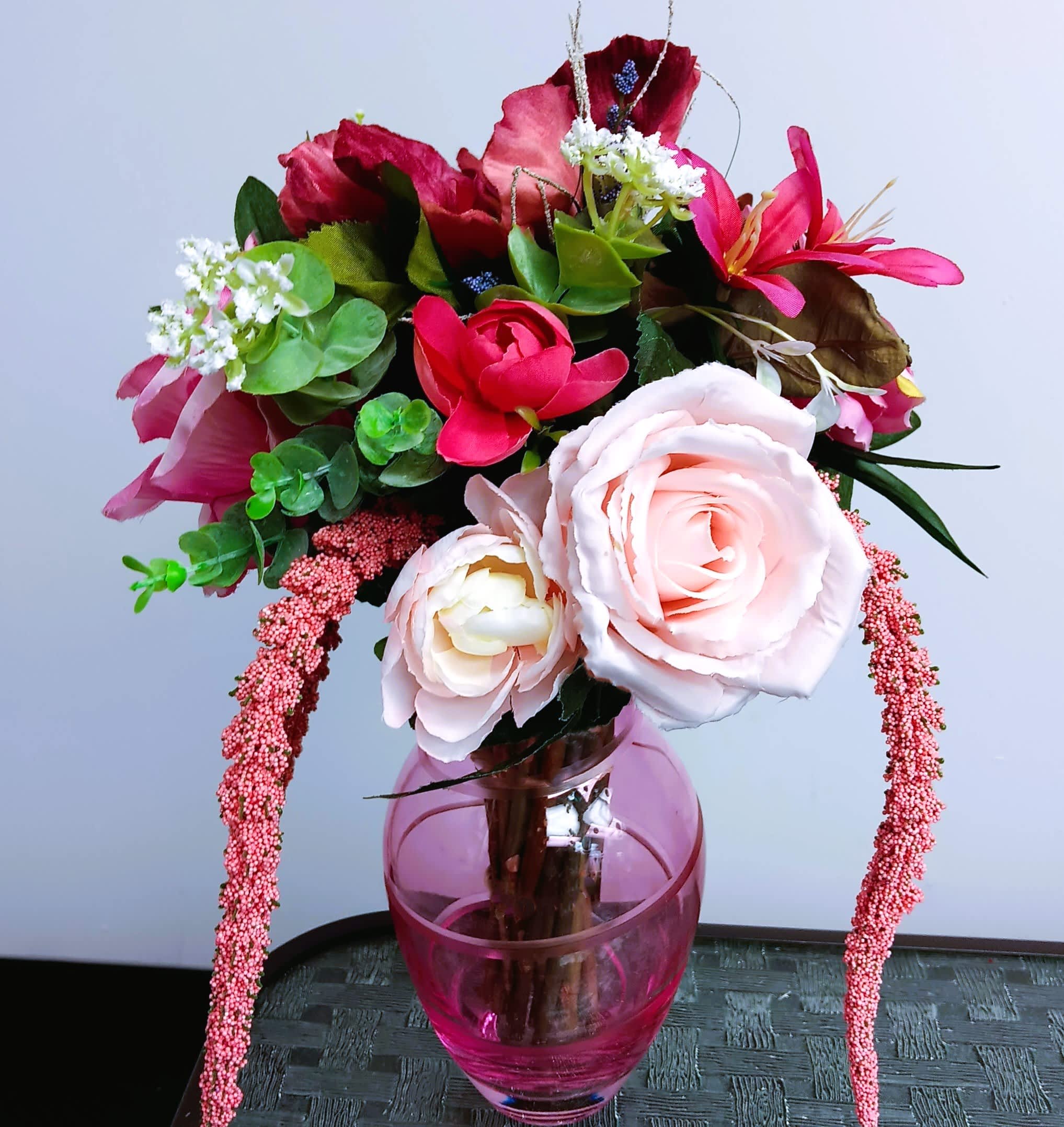 Pink and red floral arrangement in a pink glass vase