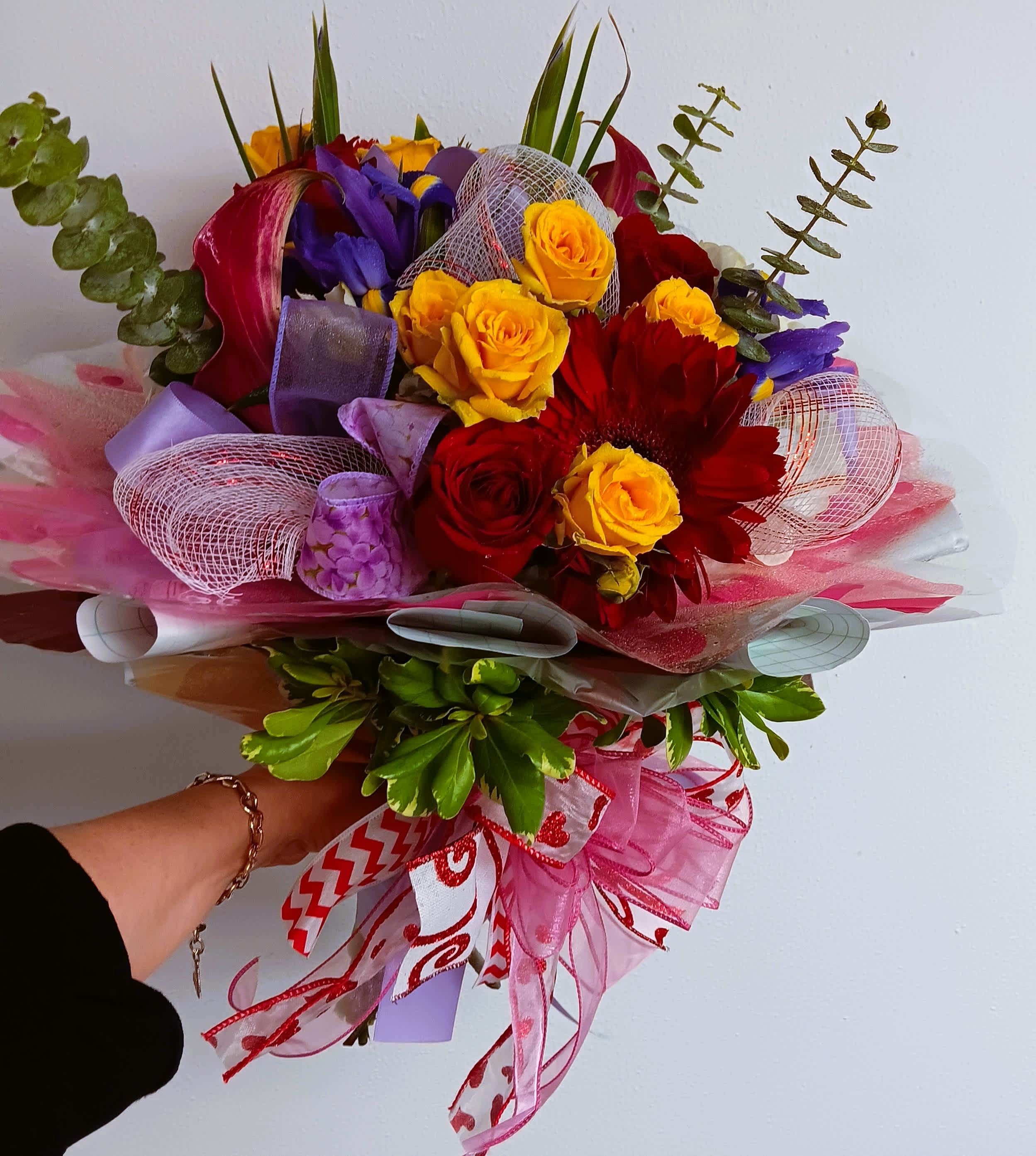 Handheld bouquet of red, yellow, and purple flowers with pink ribbon wrap