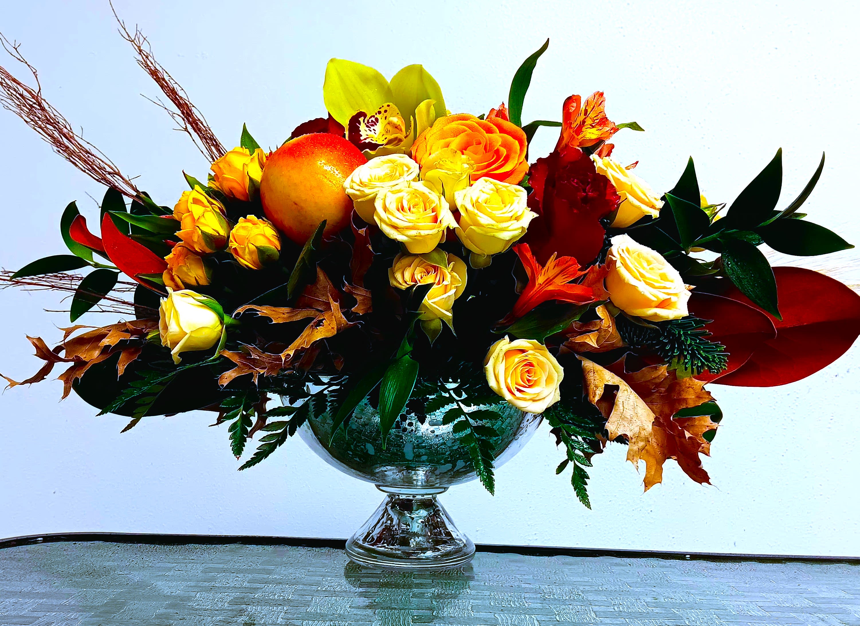 Bouquet of yellow and orange roses in a glass vase with autumn leaves
