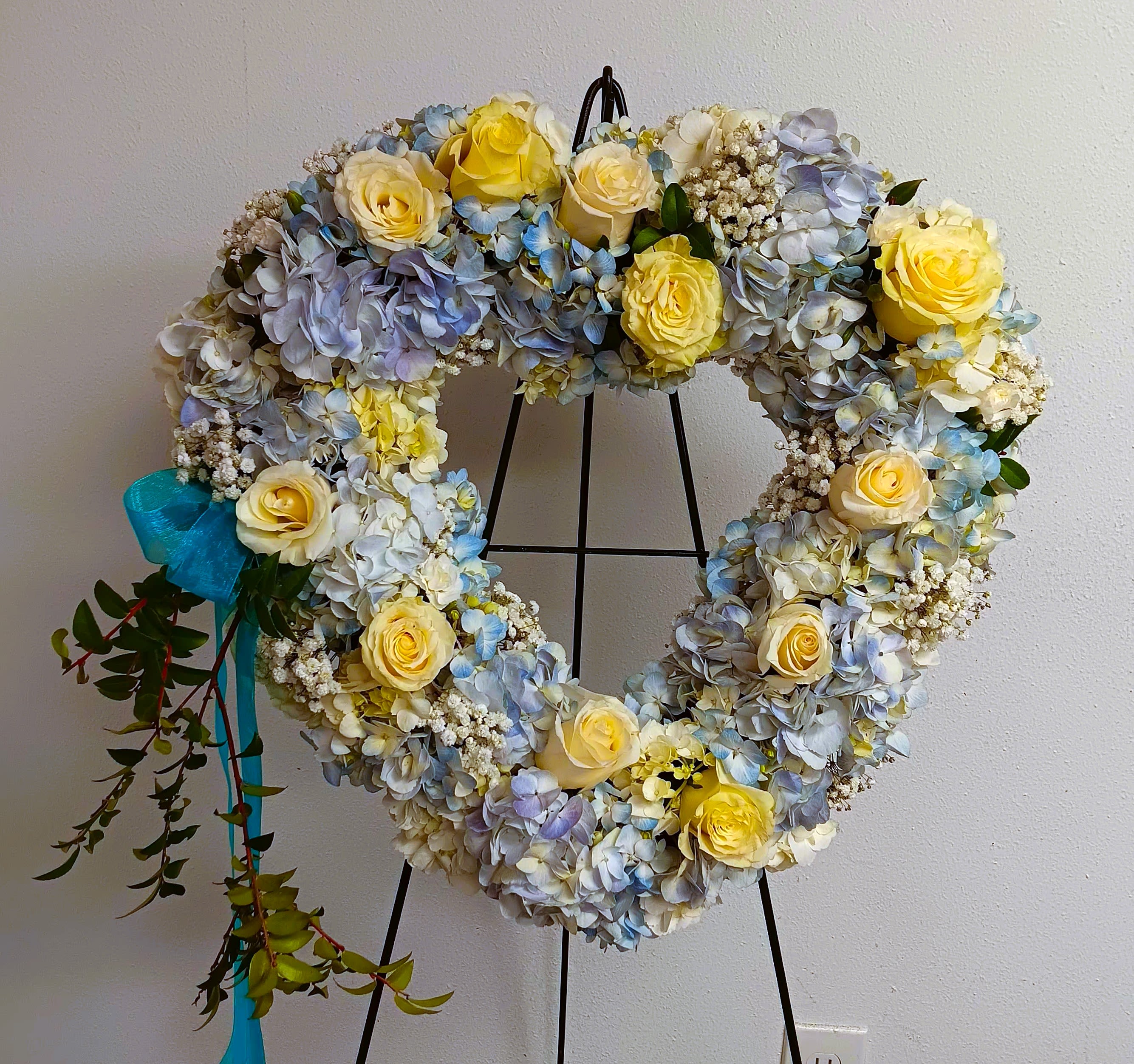 Heart-shaped floral wreath with yellow roses and blue hydrangeas on a stand