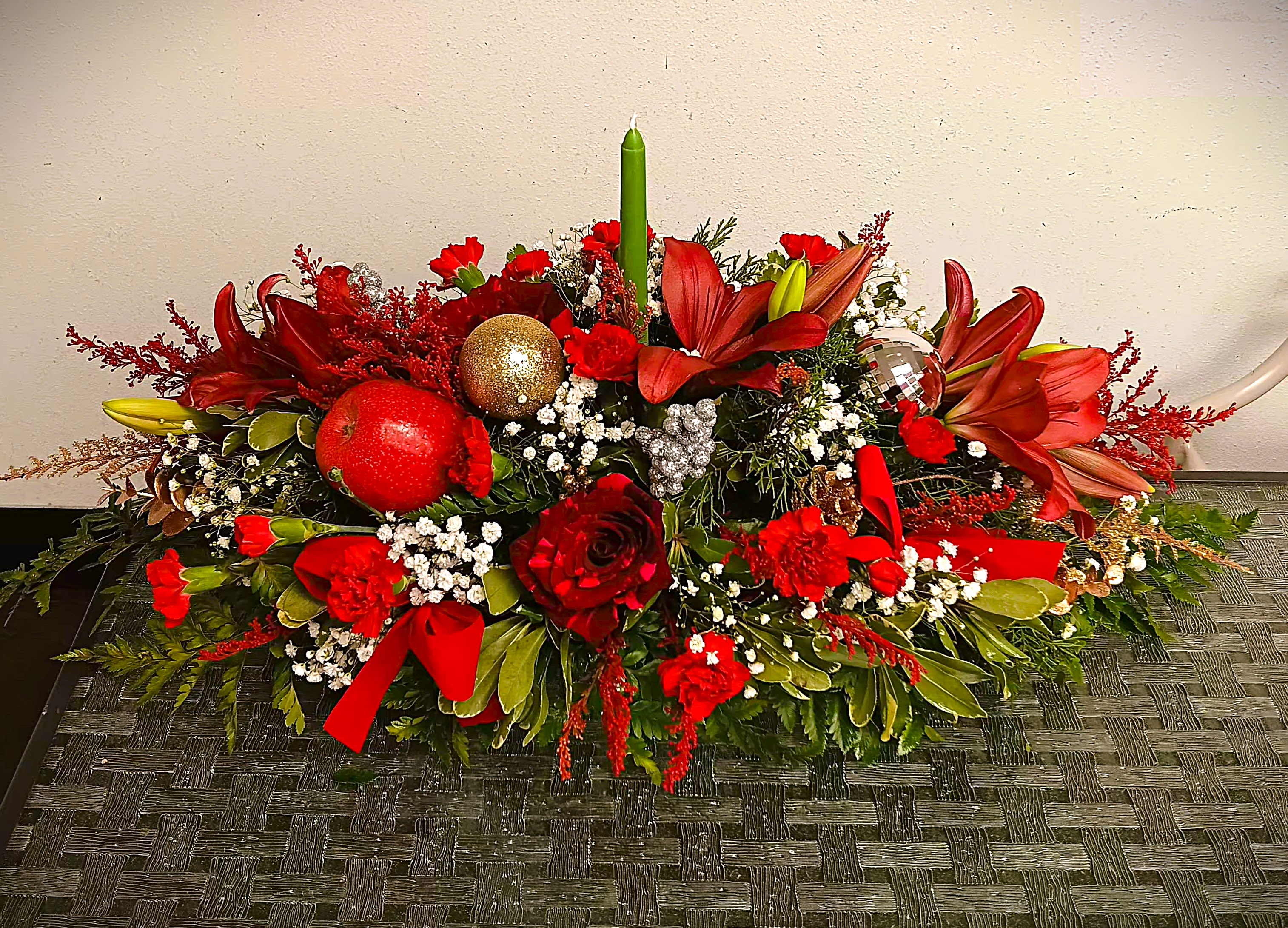Low floral centerpiece with red lilies, roses, ornaments, and a green taper candle