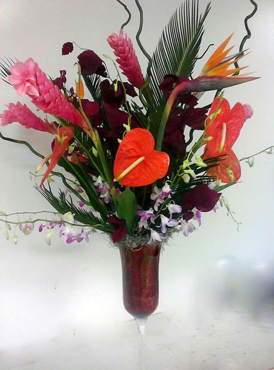 Tropical flower arrangement in a tall glass vase with orange anthuriums and pink blooms