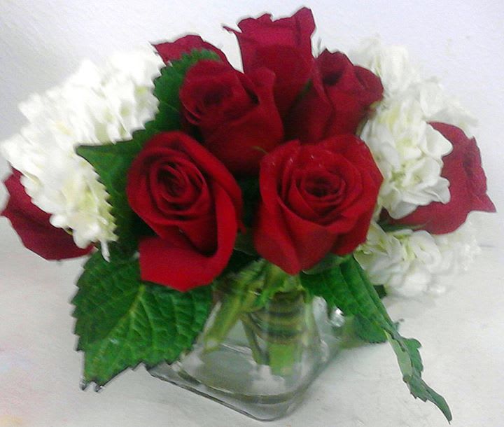 Red roses and white flowers arranged in a clear glass vase